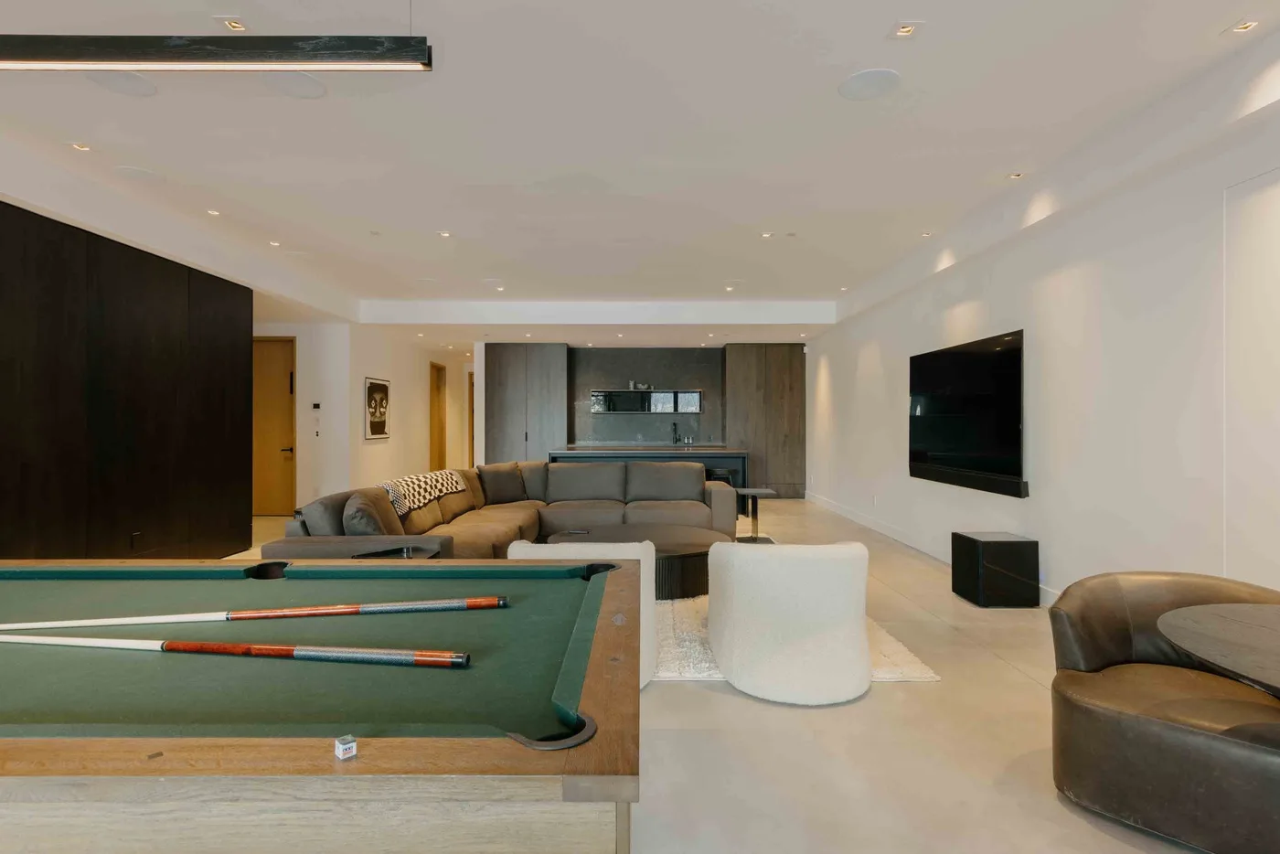 Una sala de estar moderna con mesa de billar, asientos y un televisor montado en la pared.