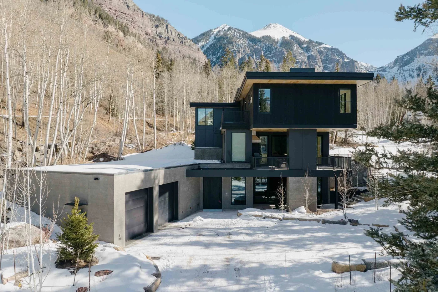 Una casa moderna se encuentra en un paisaje montañoso nevado entre árboles sin hojas.