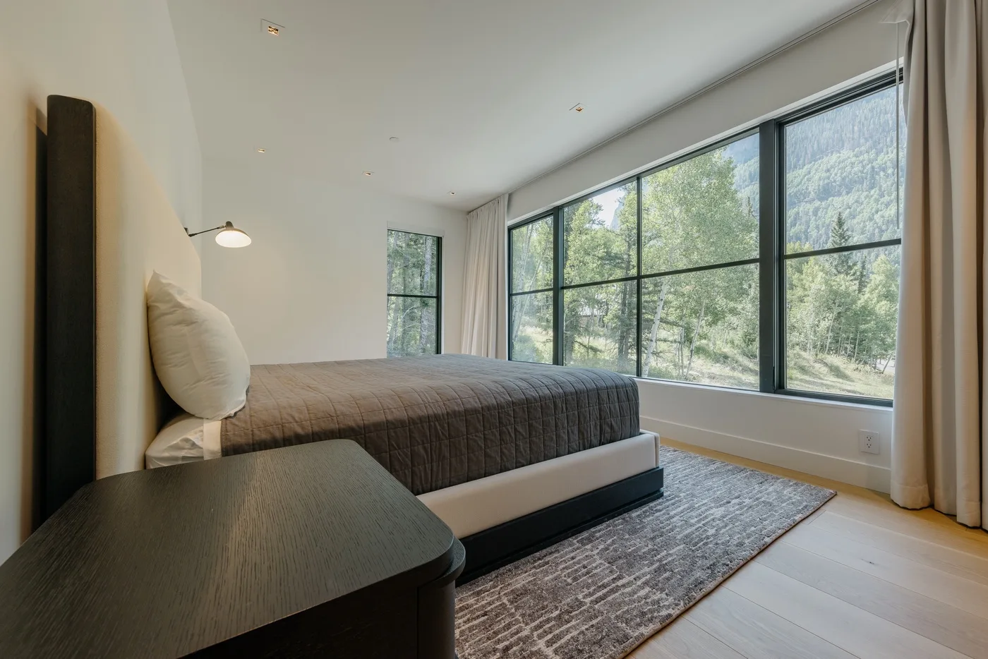 Un dormitorio con una cama junto a grandes ventanas con vistas a un paisaje verde.