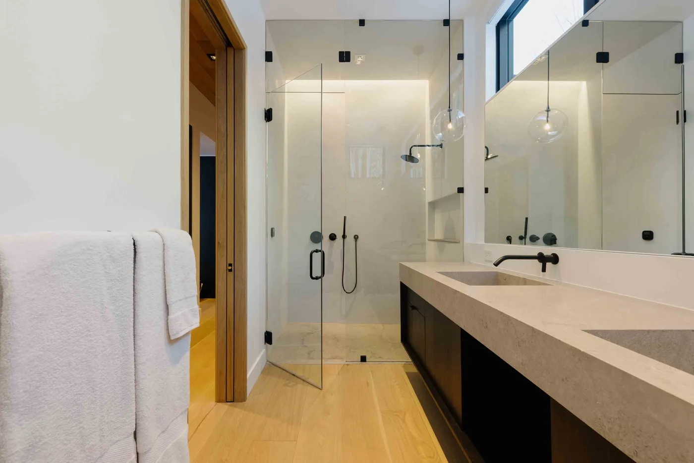 Un baño moderno y luminoso con una ducha de vidrio y un tocador largo.