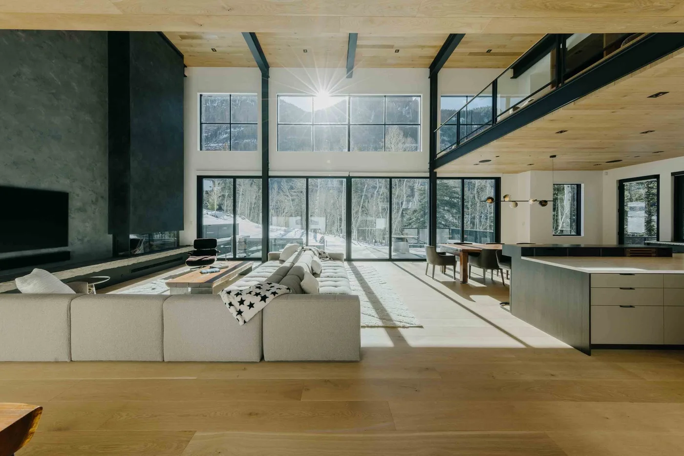 Sala de estar y cocina de planta abierta, iluminadas por grandes ventanas y con asientos.