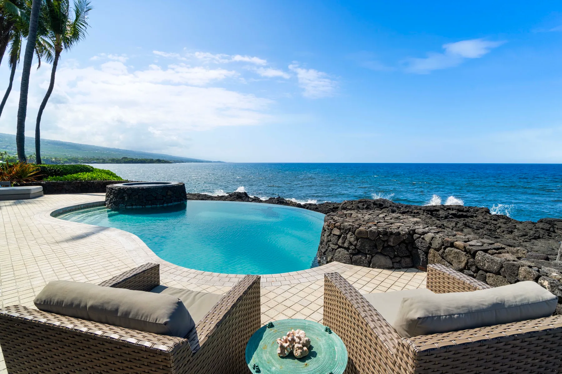 Una piscina junto al mar y un patio miran al océano, con asientos acolchados en primer plano.