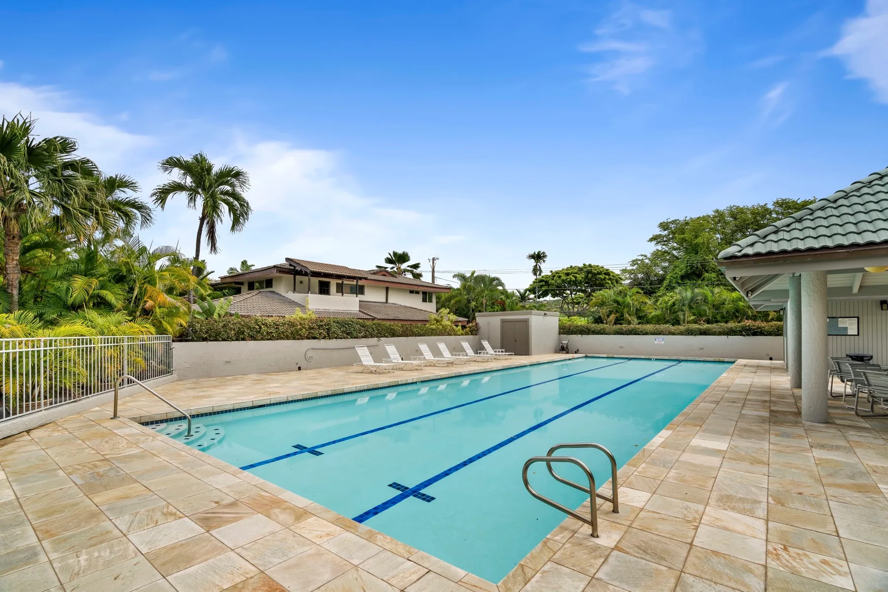 Una piscina con carriles está rodeada por una terraza de baldosas y vegetación tropical.