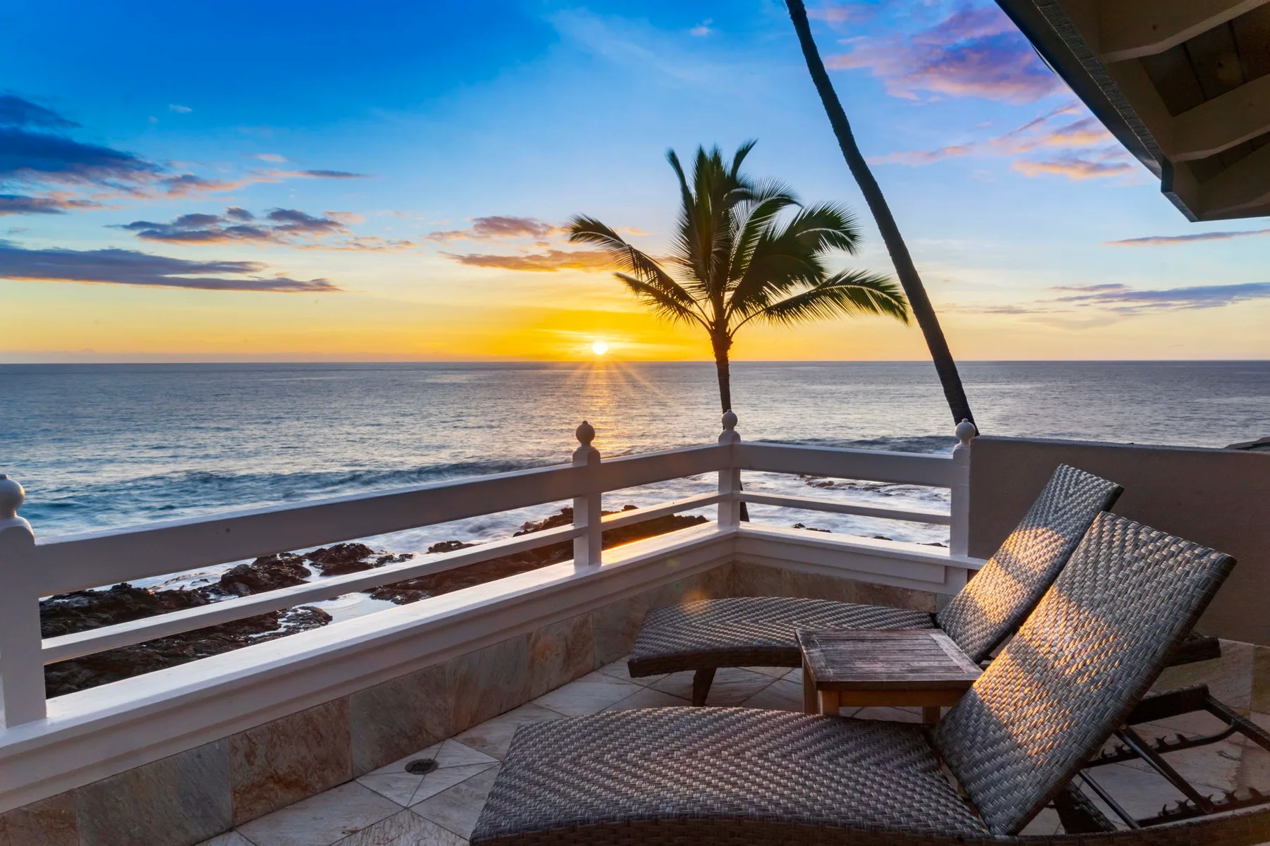 Una terraza frente al mar mira hacia el agua y una palmera al atardecer.
