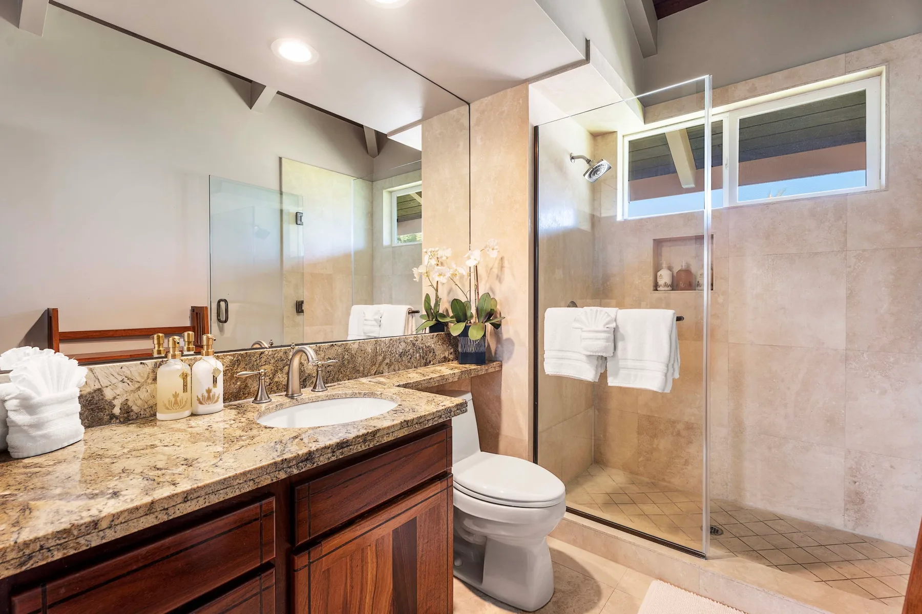 Un baño con un tocador largo, lavabo y ducha con mampara de vidrio.