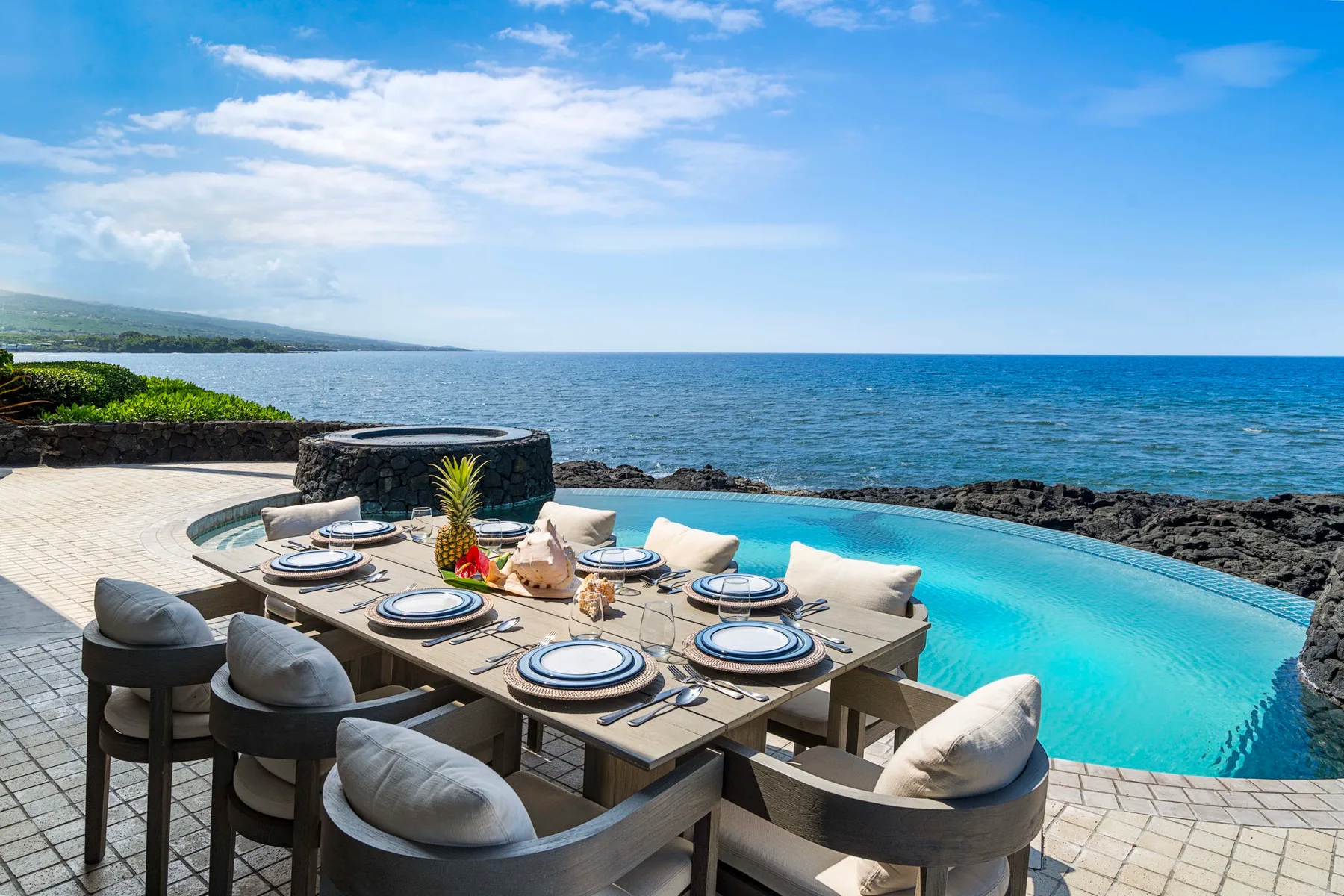 Una zona de comedor al aire libre junto a una piscina turquesa con vistas al mar.