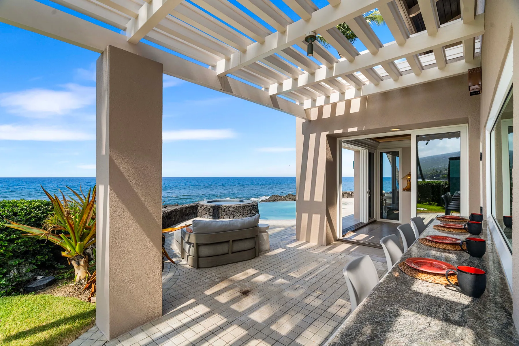 Un patio cubierto junto al mar tiene una mesa de comedor y asientos con vistas al océano.