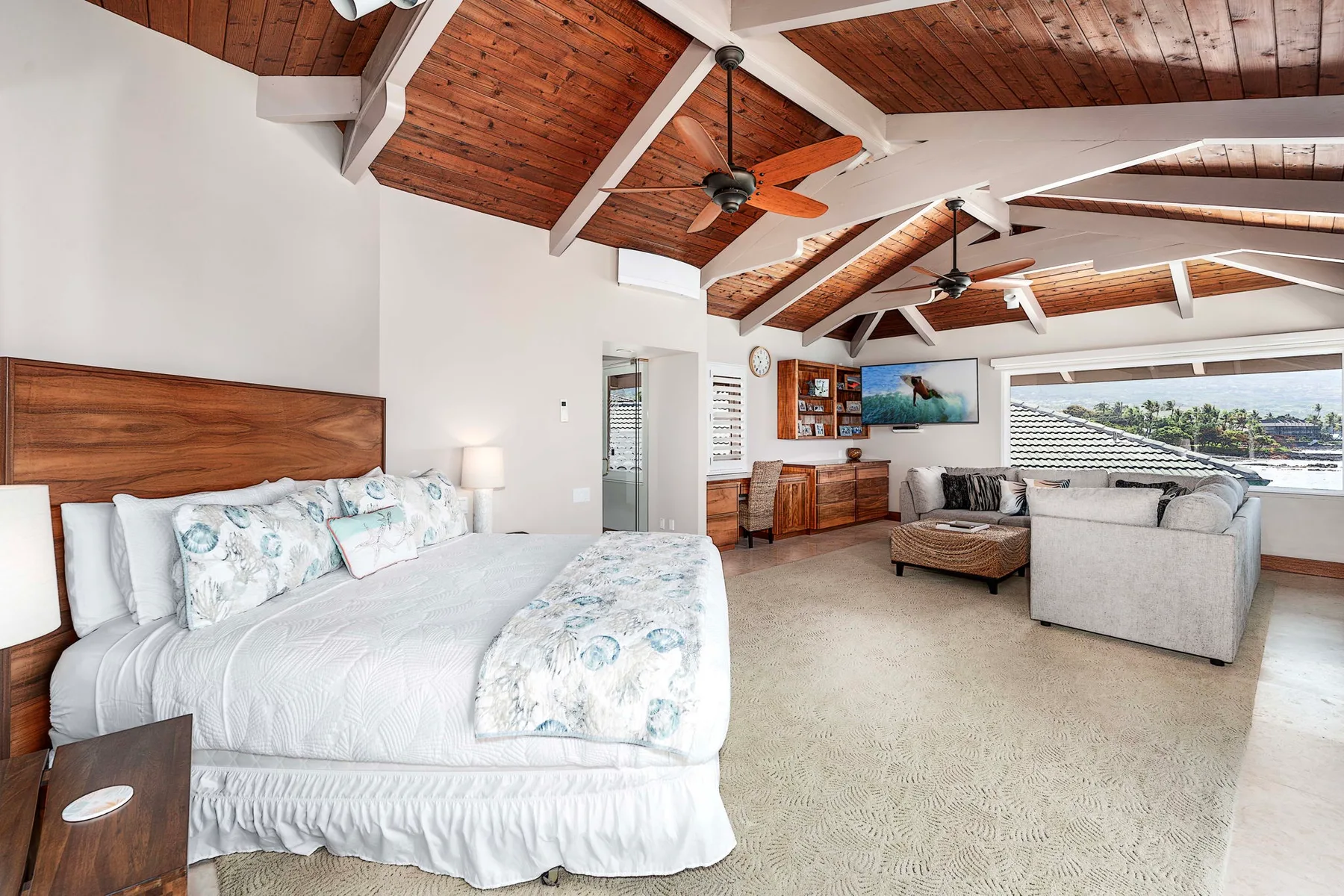 Un dormitorio luminoso y una zona de estar comparten un espacio bajo un techo alto de madera.
