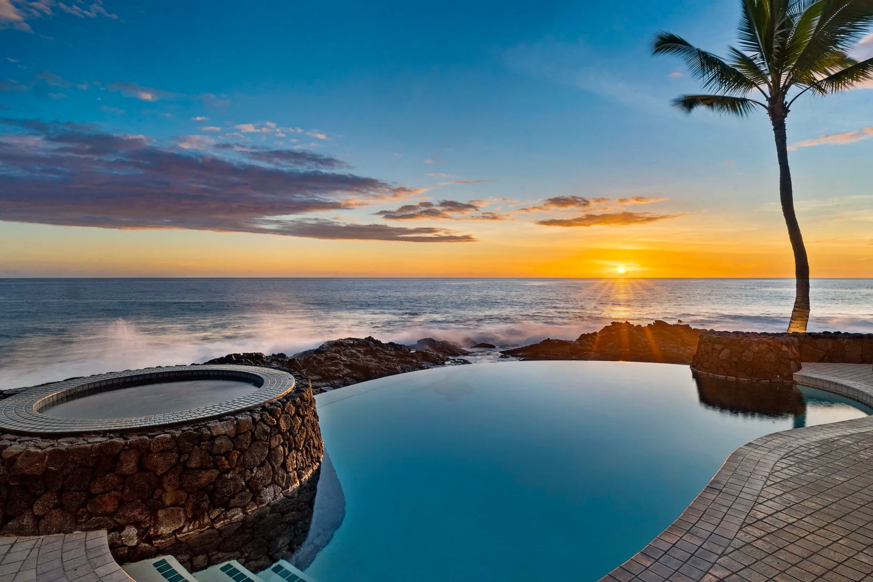 Una piscina da al océano al atardecer, con una palmera cerca.