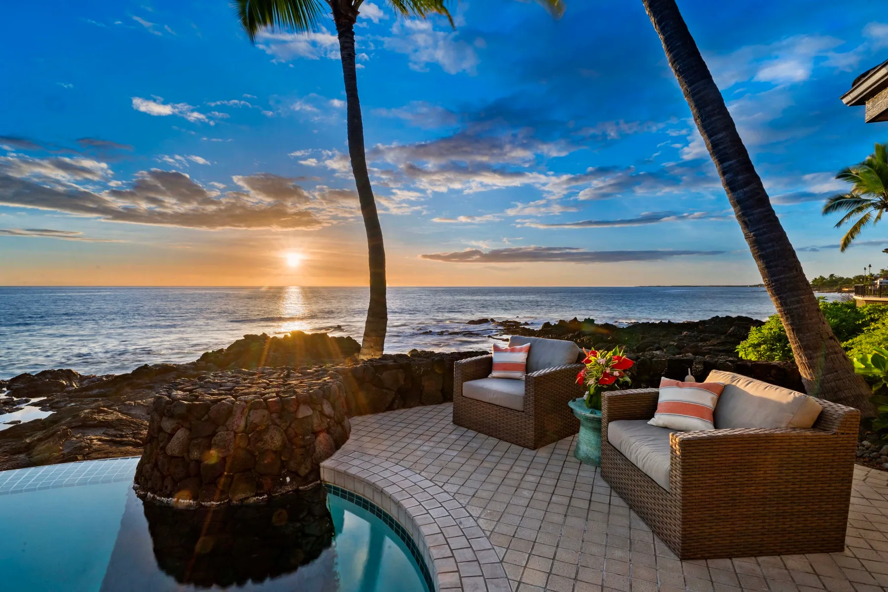 Un patio junto al mar con asientos acolchados da al océano al atardecer.