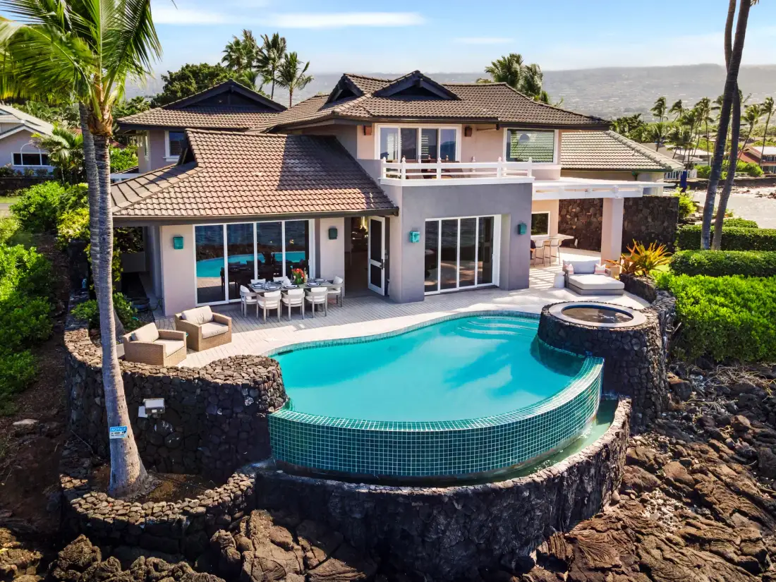 Una casa grande da a una piscina curva y un spa circular elevado.
