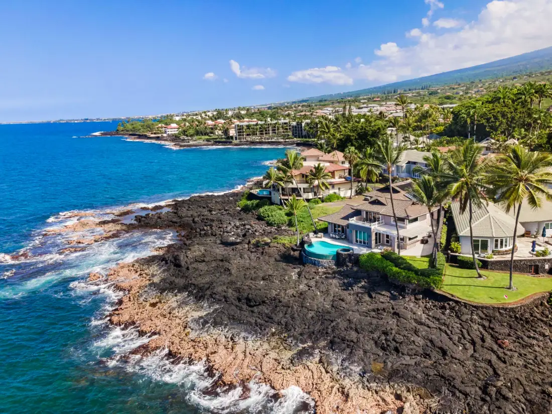 Un vecindario costero junto al mar azul, con casas y palmeras junto a una costa rocosa.