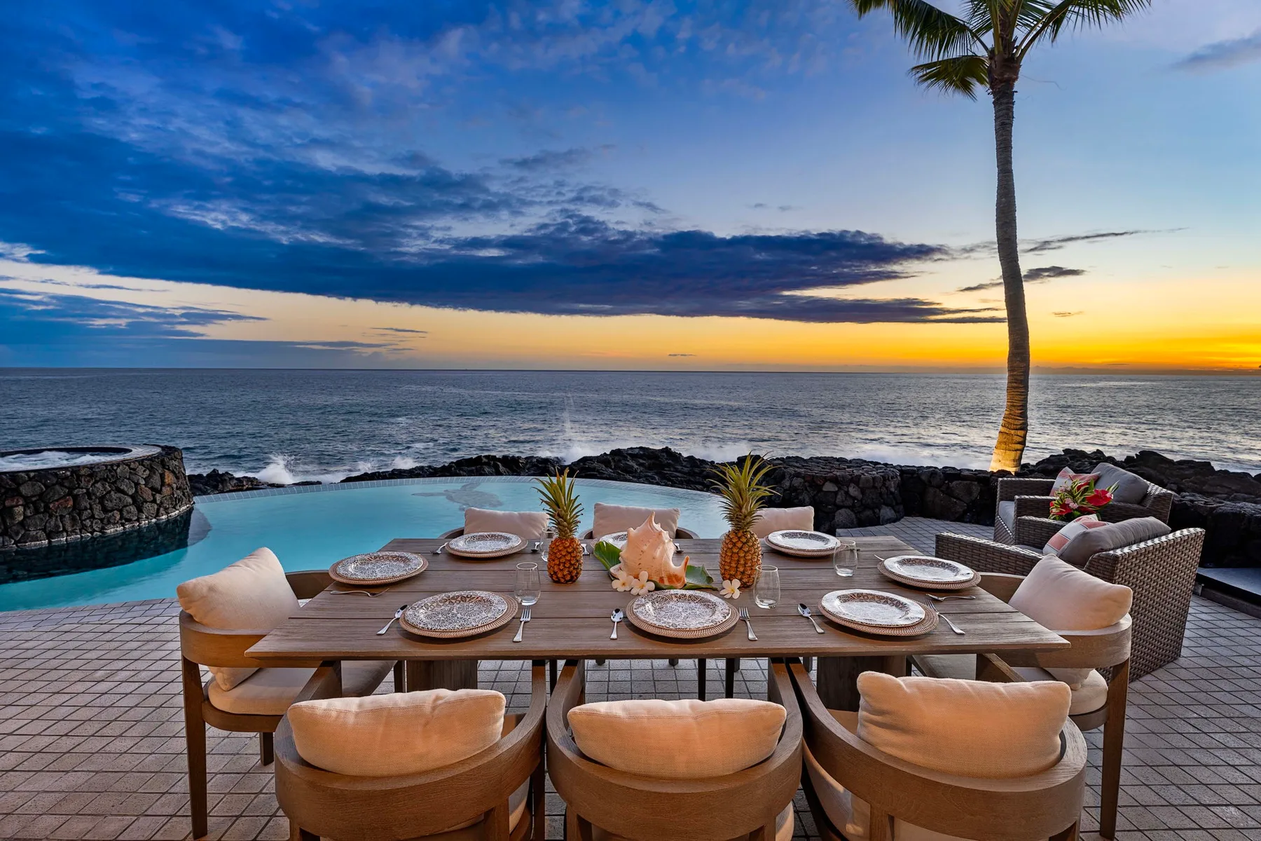 Una mesa de comedor al aire libre junto a una piscina mira al mar al atardecer.