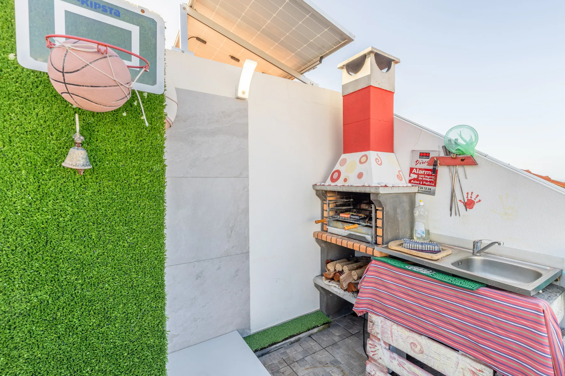 An outdoor barbecue area with a grill, counter, and basketball hoop.