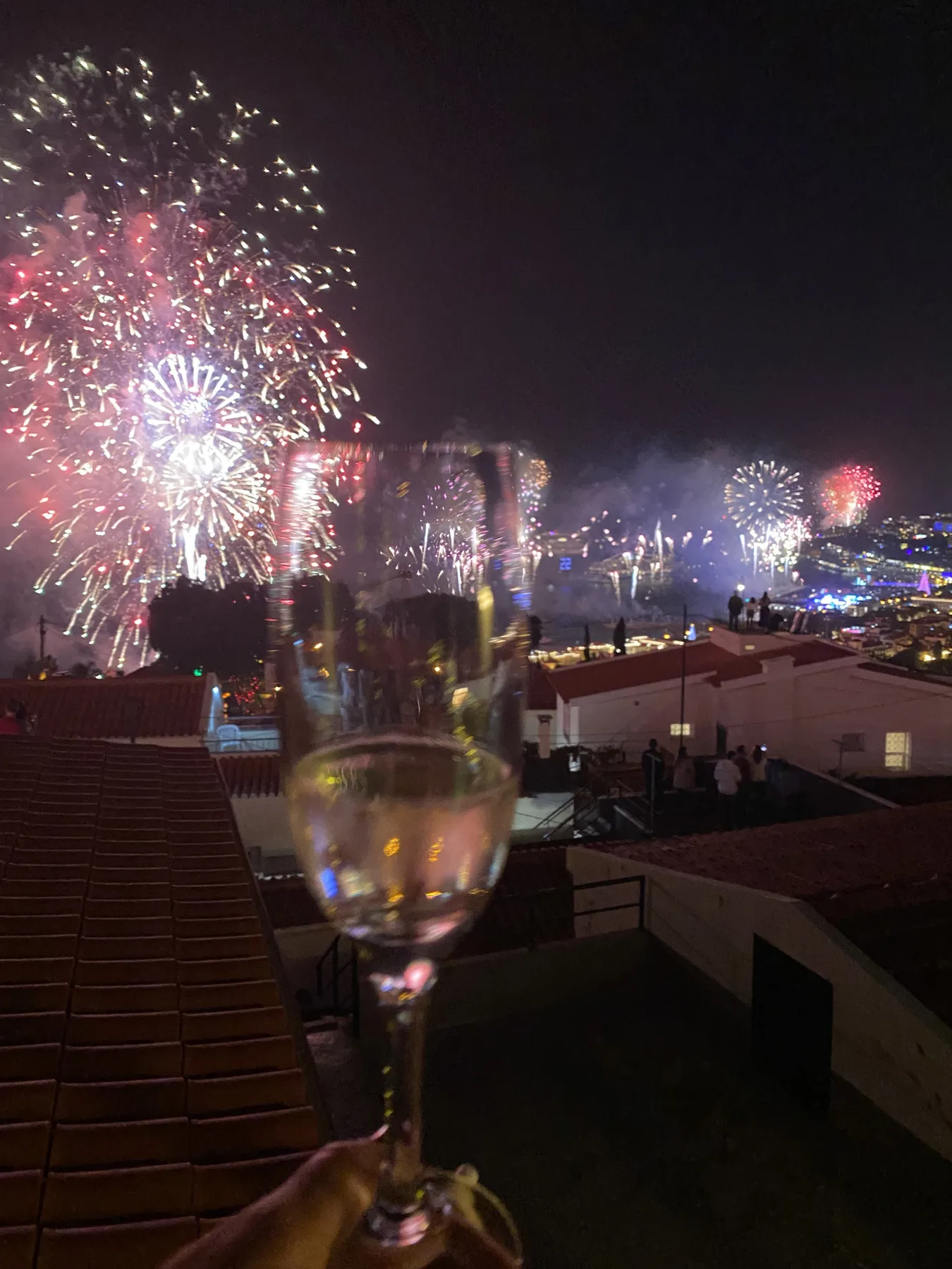 Fireworks light up the night sky above rooftops, viewed from a terrace.