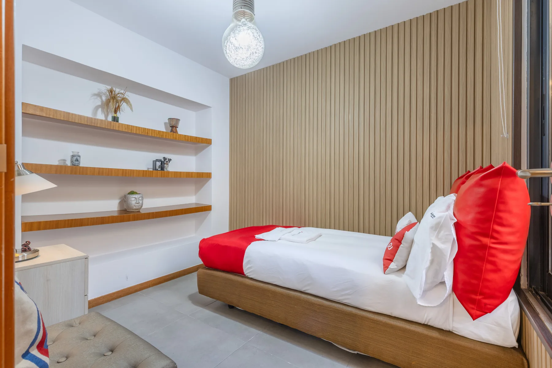 A bedroom with a bed beside built-in shelves and a vertical wood-paneled wall.