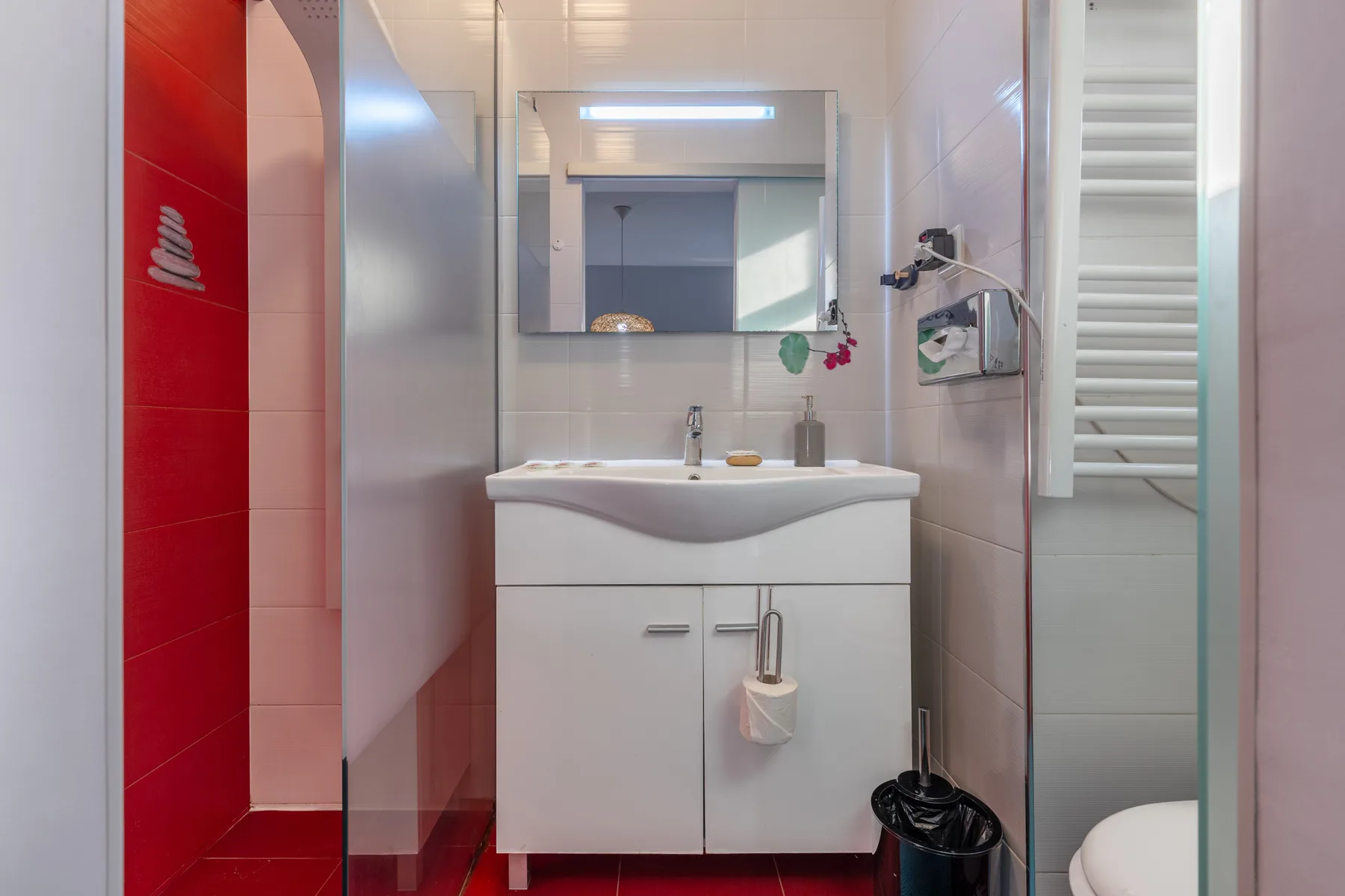 A tiled bathroom with a sink, mirror, and glass shower partition.