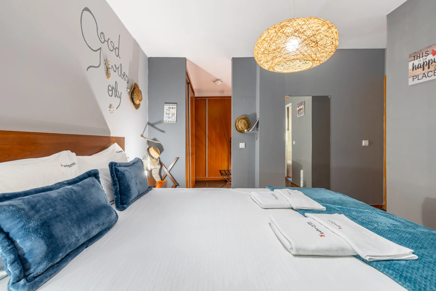 Bedroom with a large bed, blue pillows, and a woven pendant light.