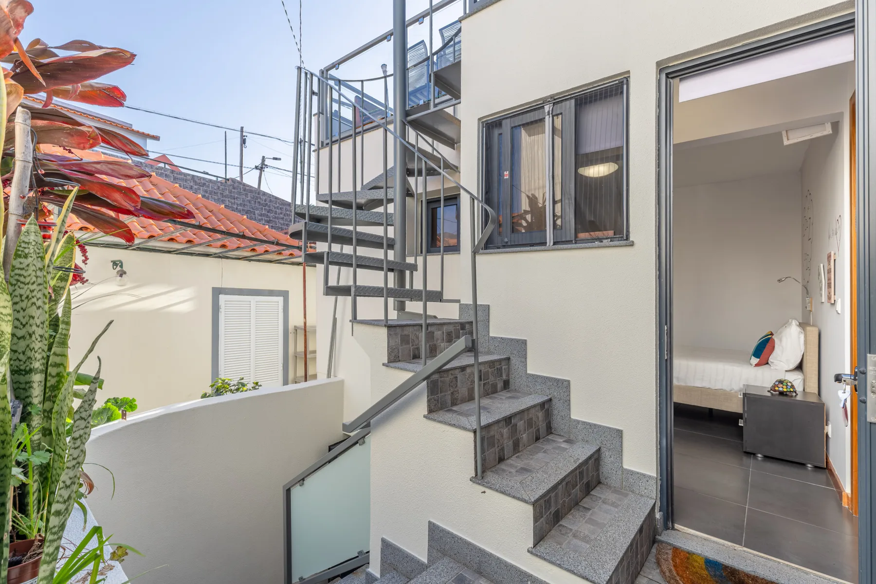 An exterior staircase beside an open bedroom doorway, with a bed visible inside.