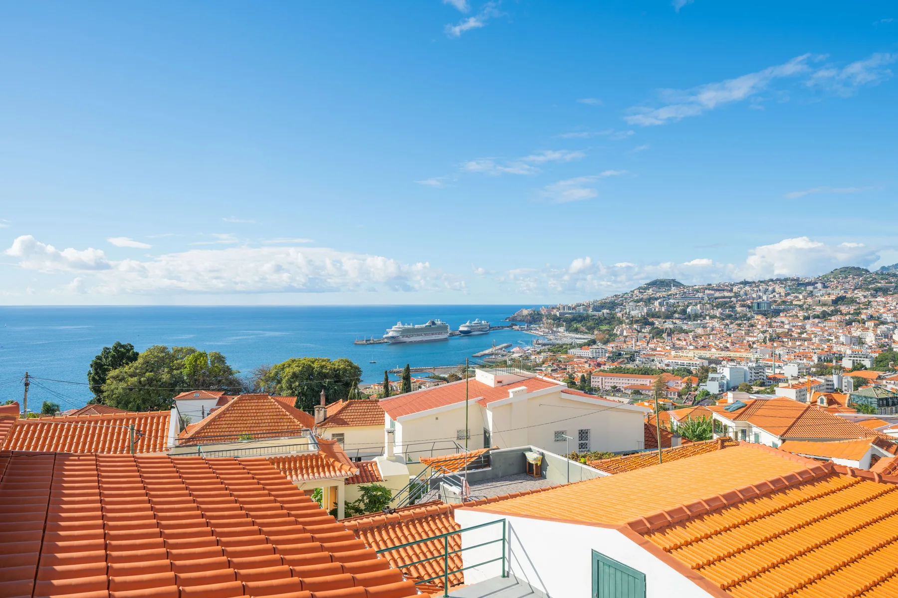 A coastal cityscape overlooks the sea, with red-tiled rooftops in the foreground.