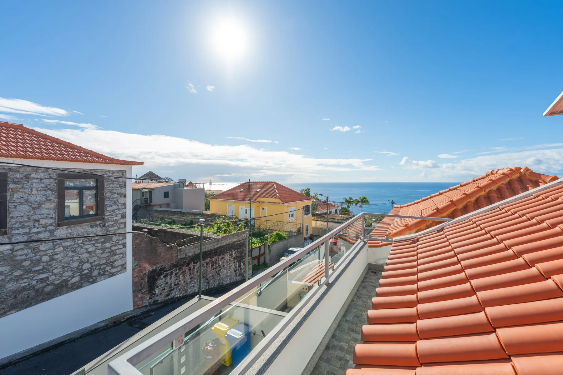 A rooftop terrace overlooks nearby houses and the ocean under a sunny sky.