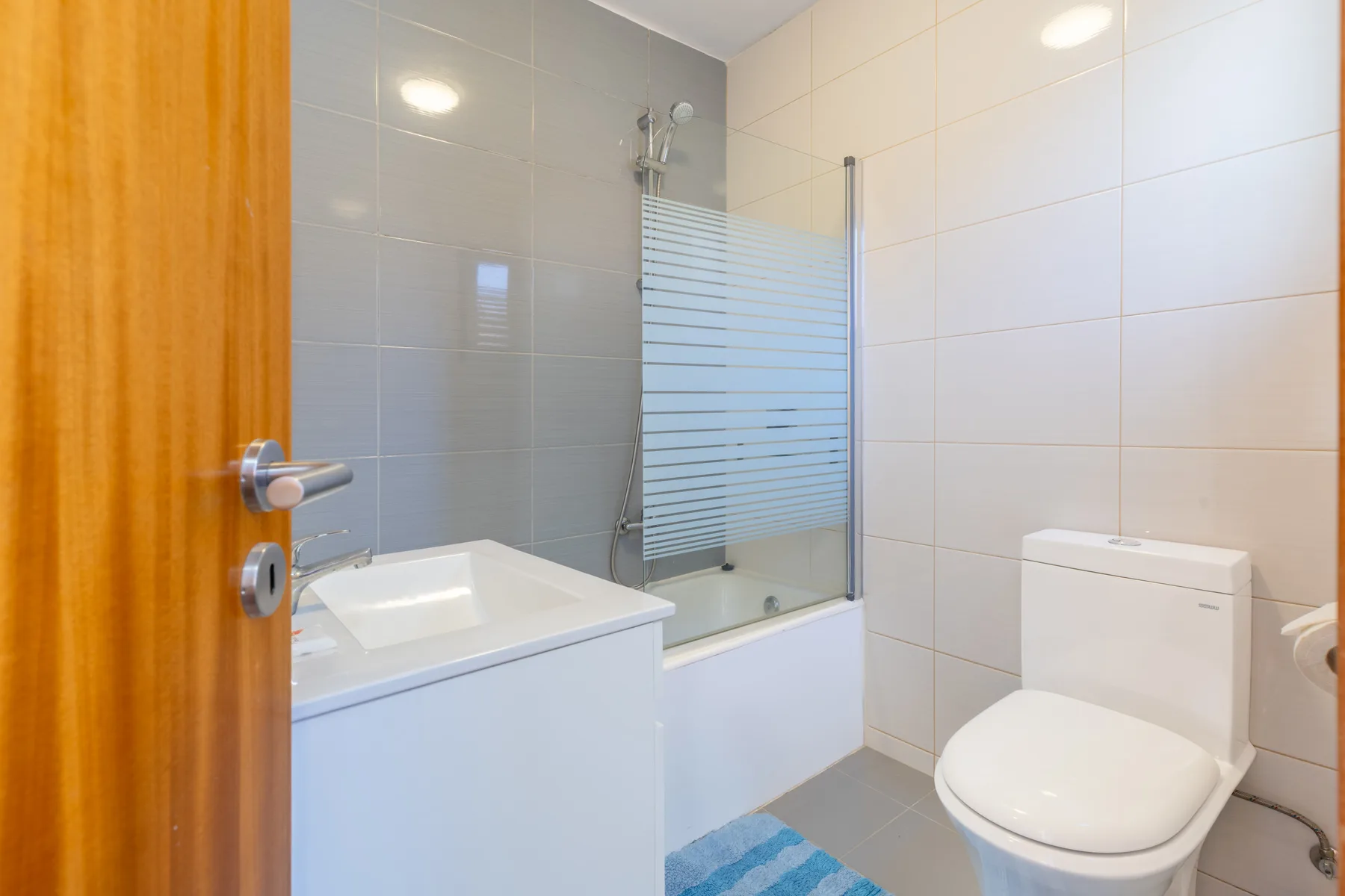 A tiled bathroom with a bathtub, glass shower screen, and toilet.