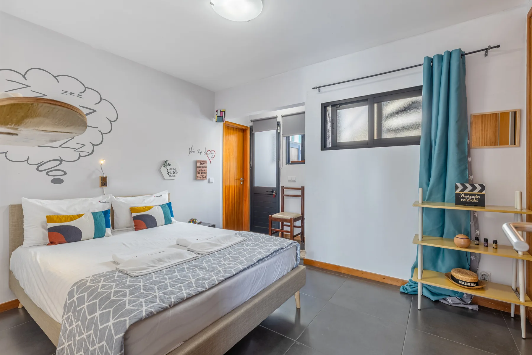 A bedroom with a double bed, colorful cushions, and a turquoise curtain.