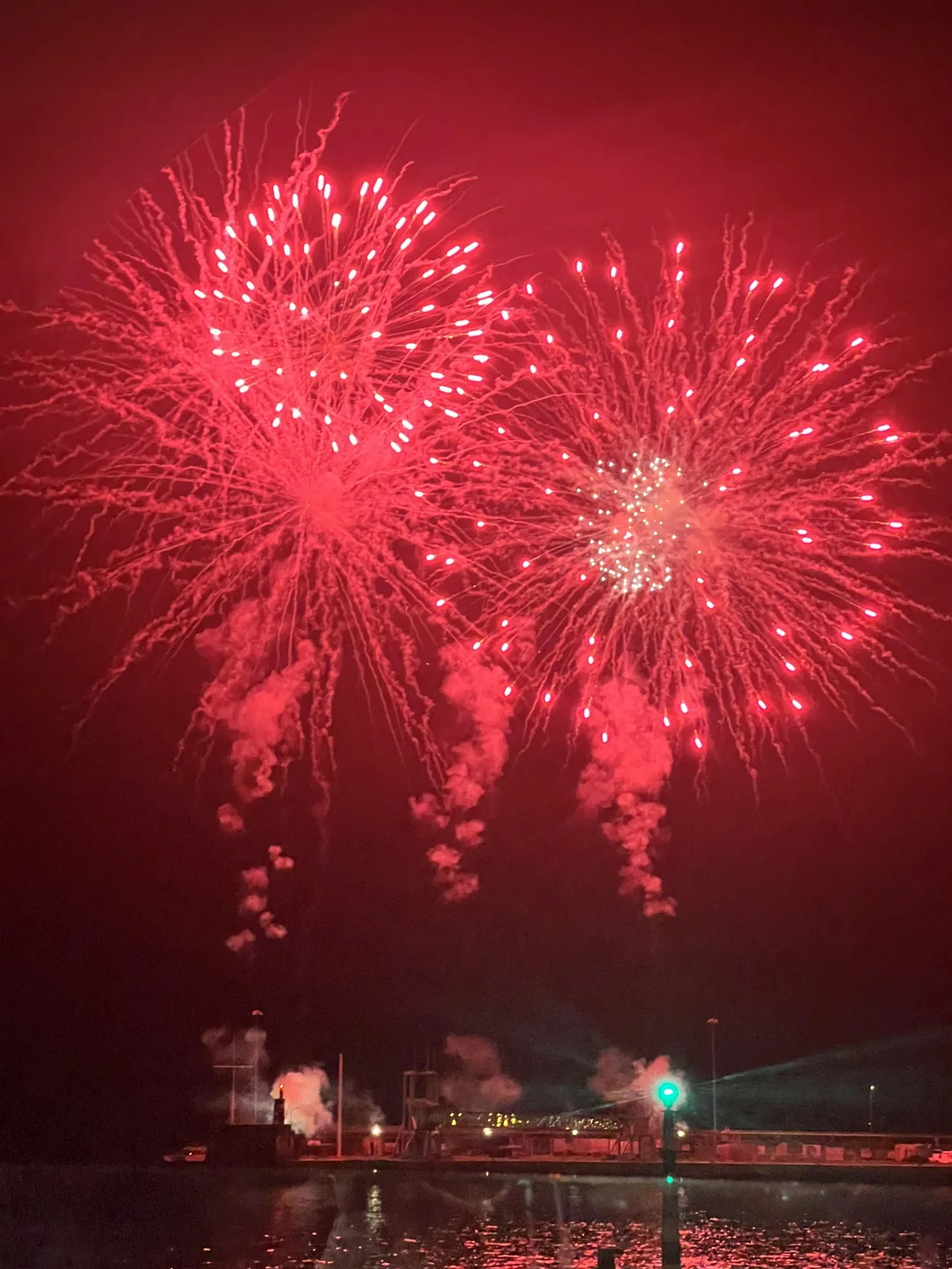 Red fireworks burst across the night sky above a waterfront.