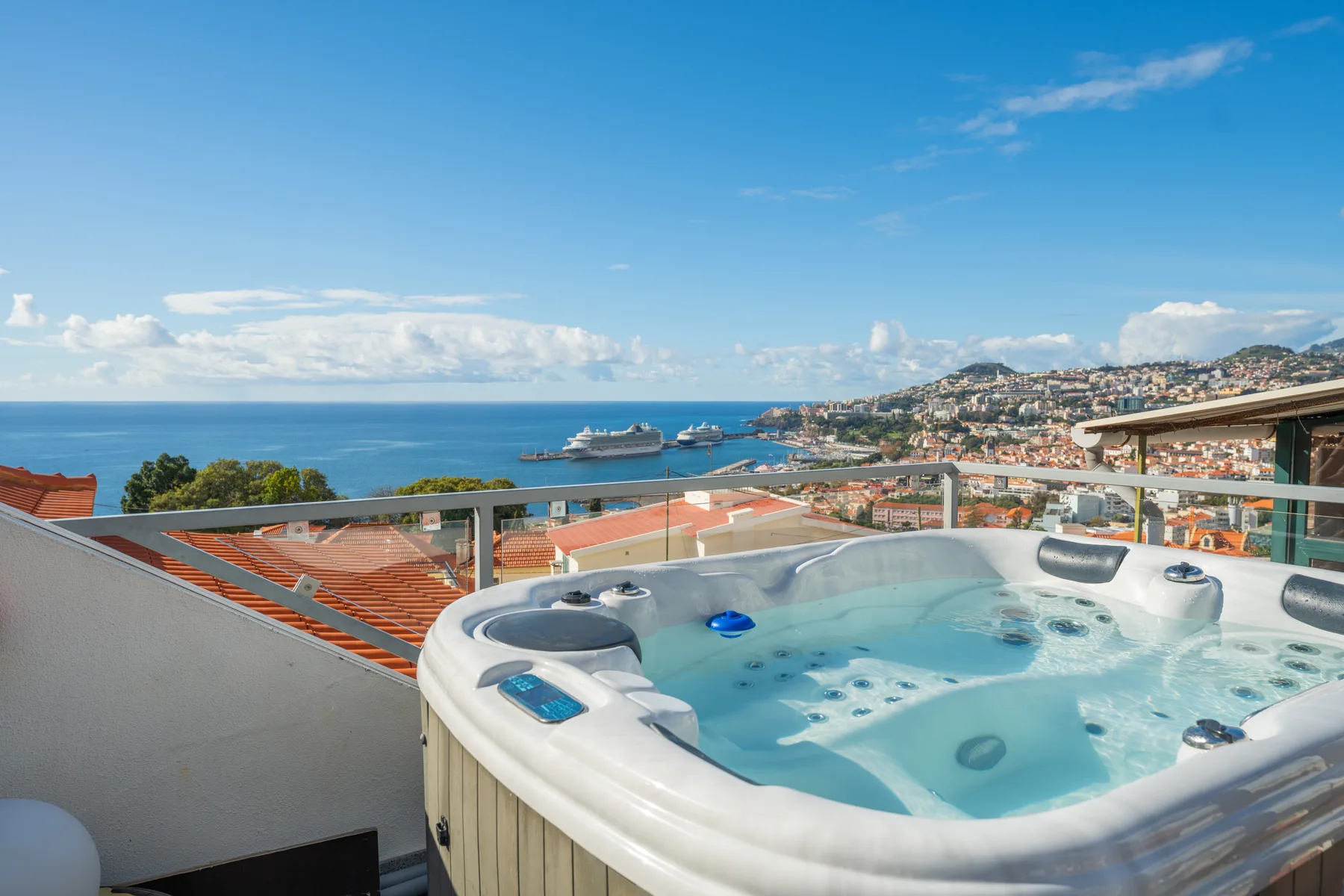 A rooftop hot tub overlooks the ocean and a coastal city.