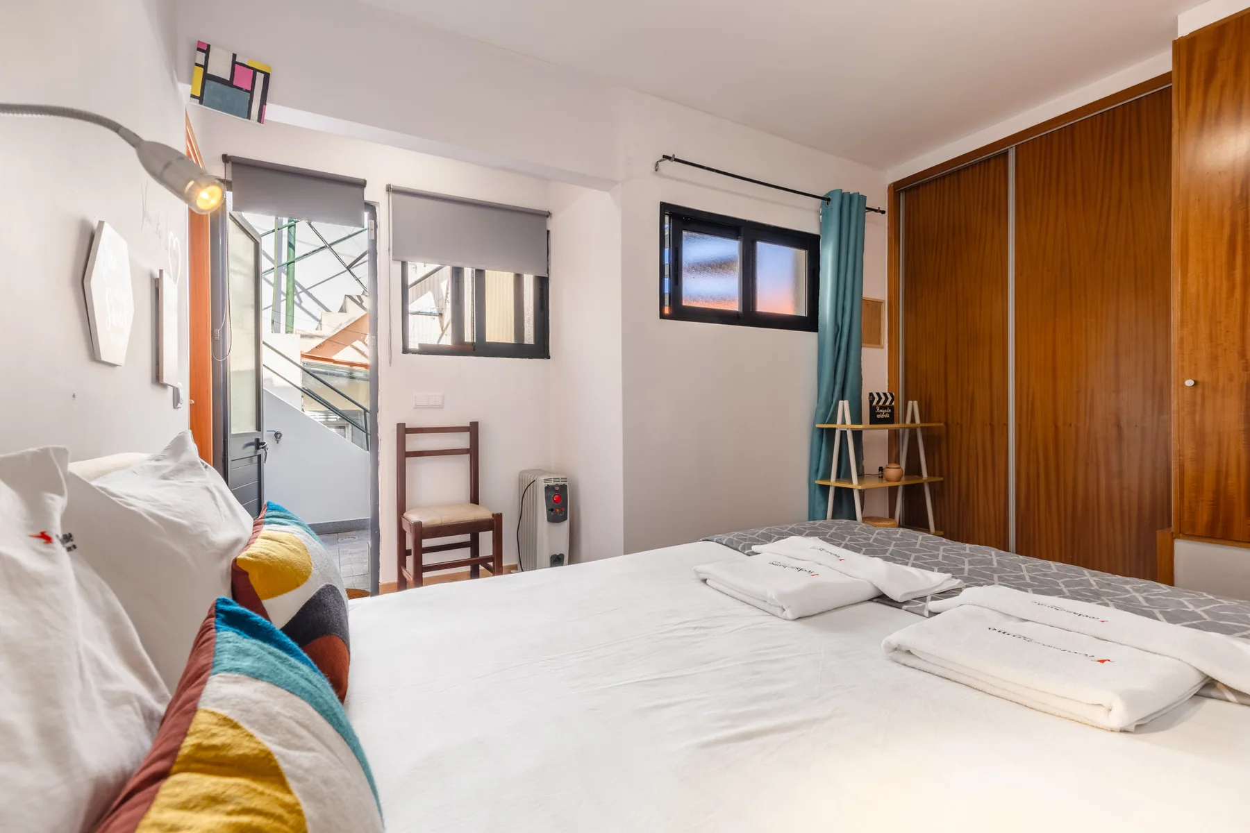 A bedroom with a bed, colorful cushions, and a wooden wardrobe.