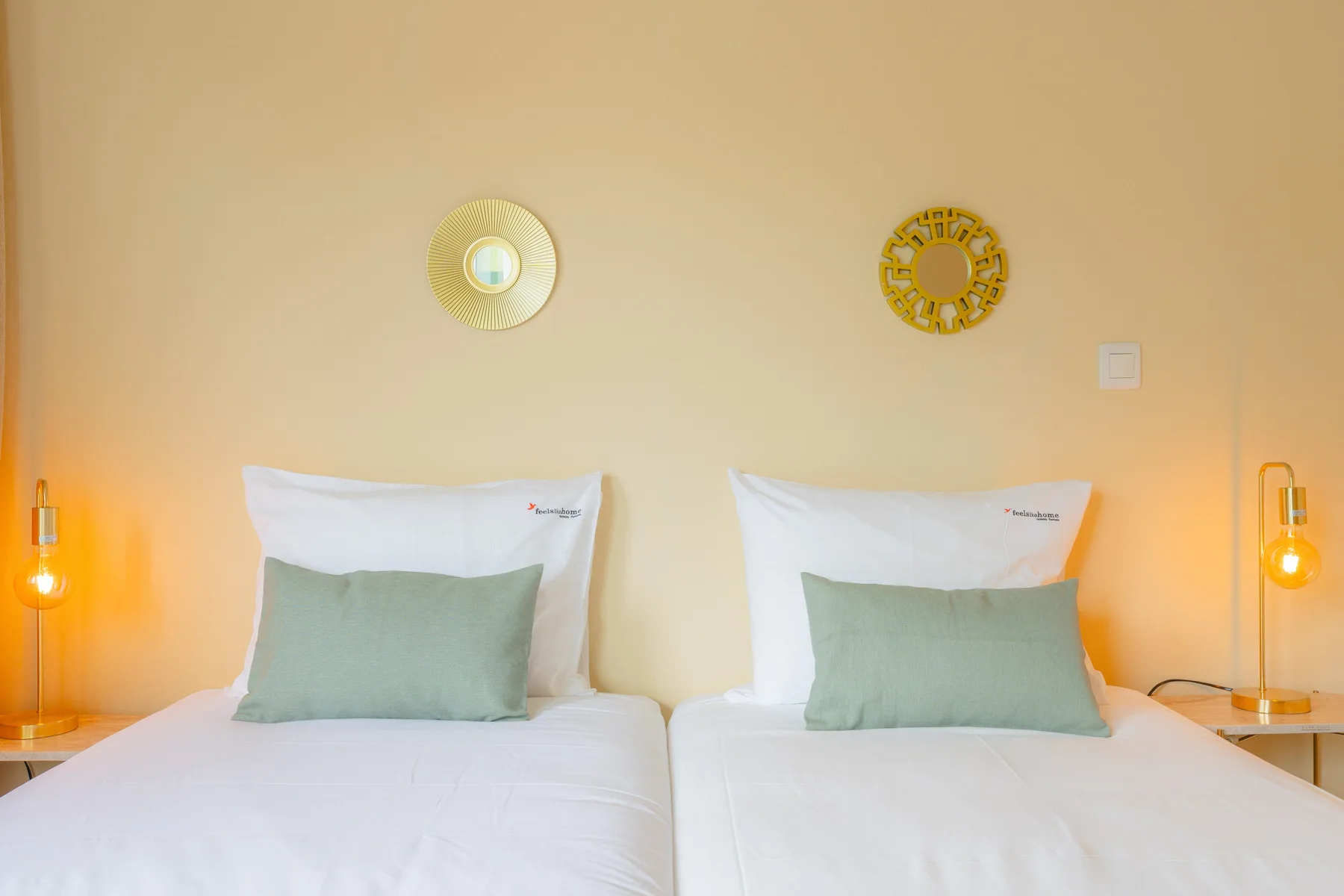 Un dormitorio con dos camas vestidas de blanco y almohadas verde claro.