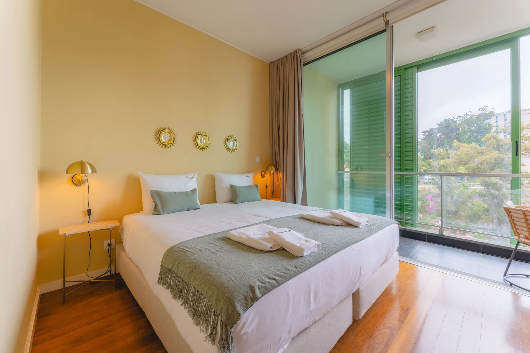 Un dormitorio luminoso con una cama bien tendida y grandes ventanas con vistas a la vegetación.