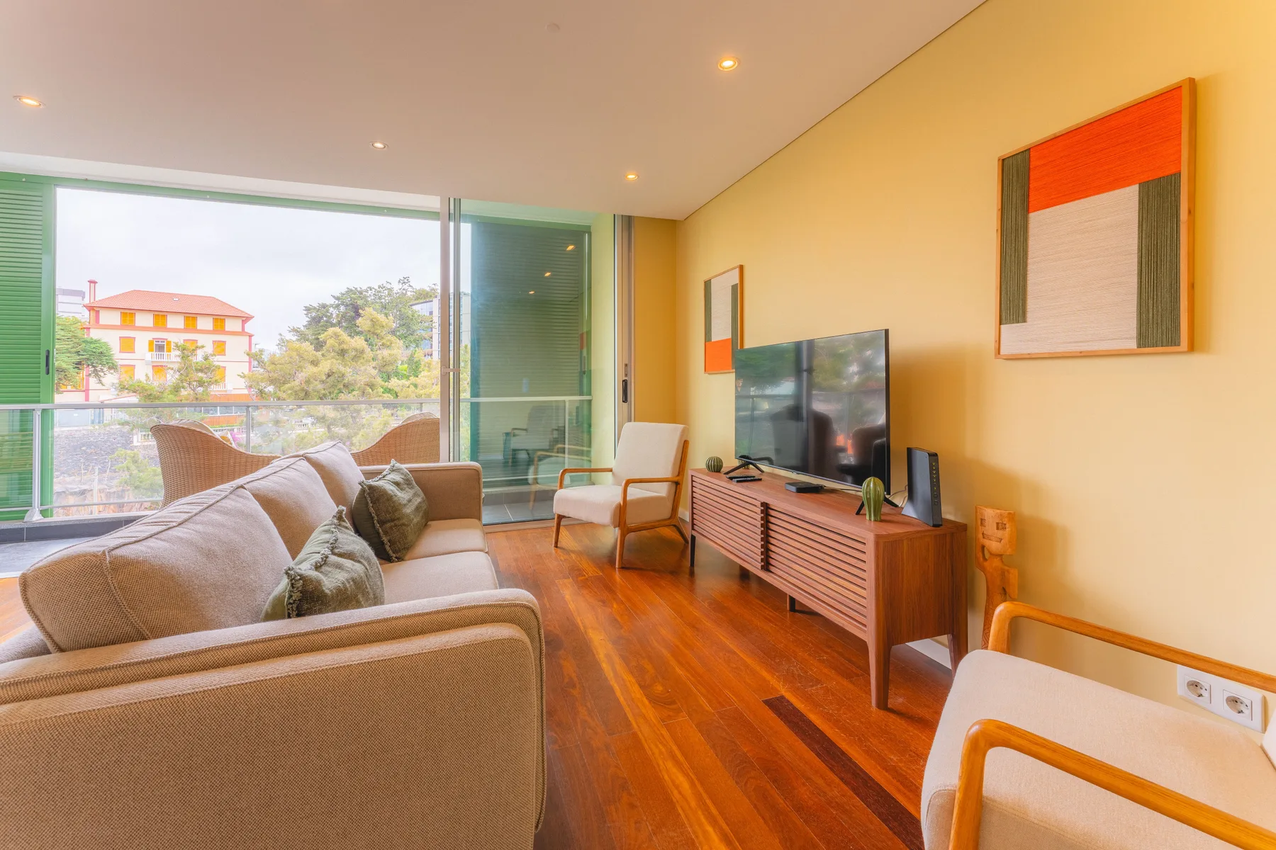 Una sala de estar con asientos, un televisor y grandes ventanas con vistas a la vegetación.