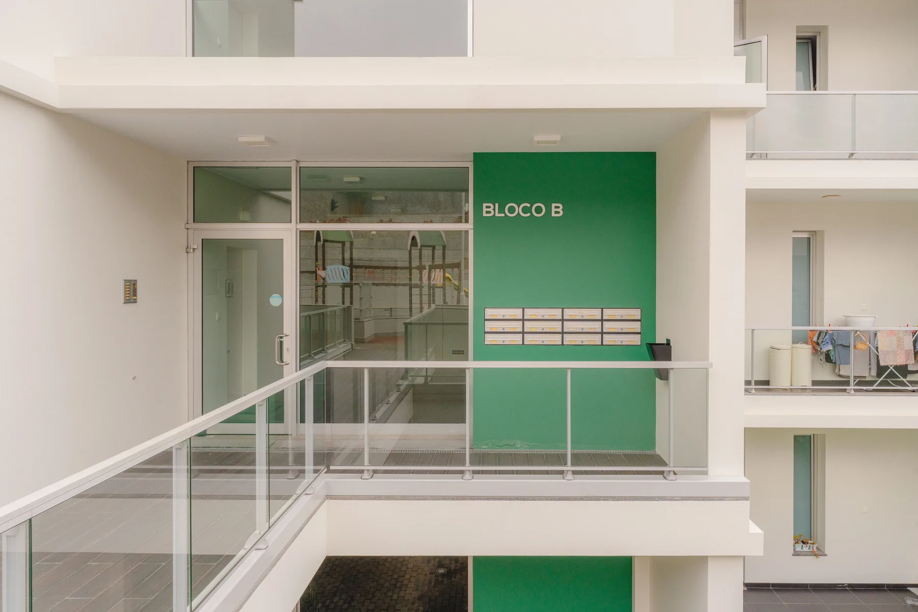 Pasillo de un edificio de apartamentos con barandillas de vidrio y una pared verde junto a la entrada.
