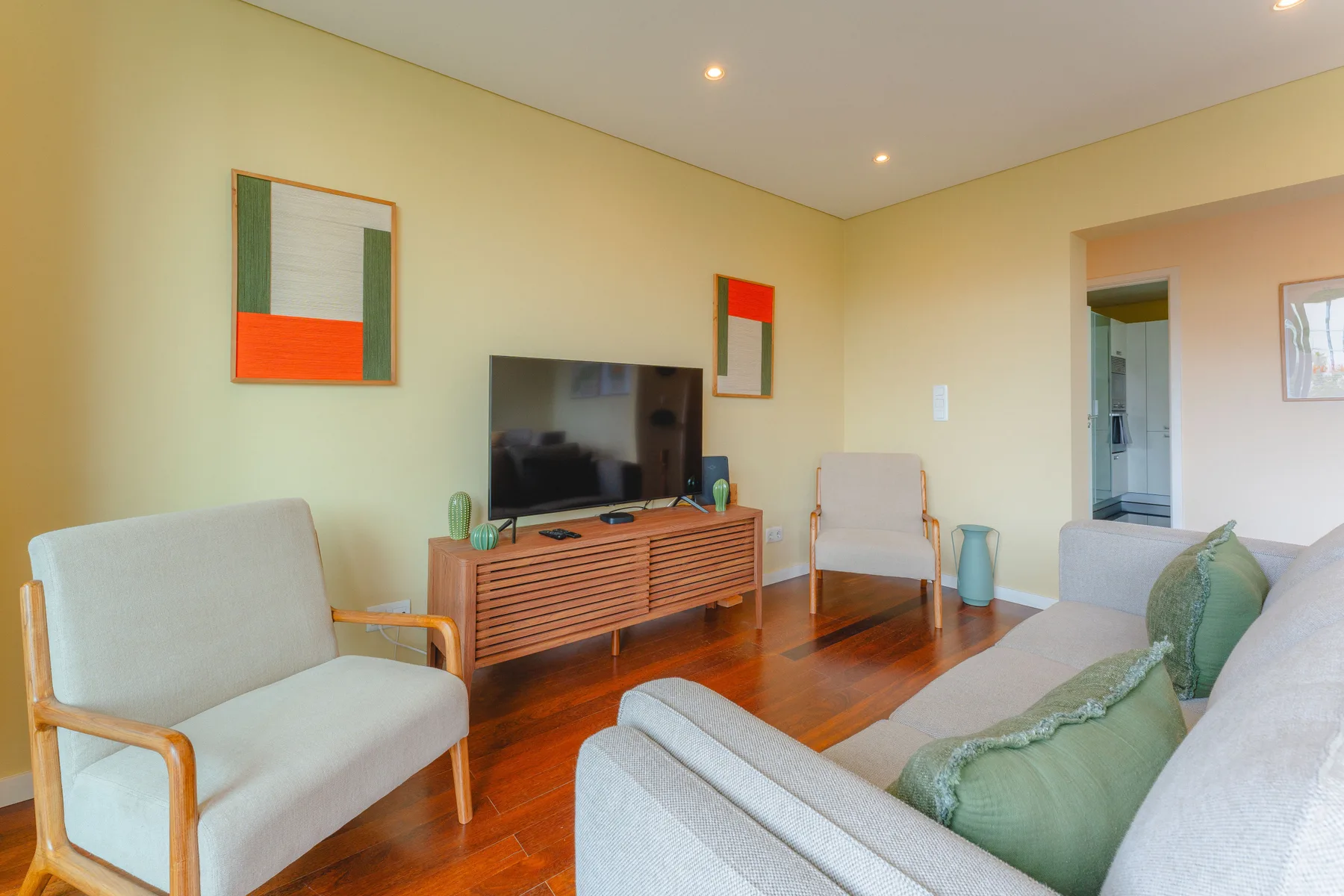 Una sala de estar con un televisor sobre un mueble de madera y asientos claros.
