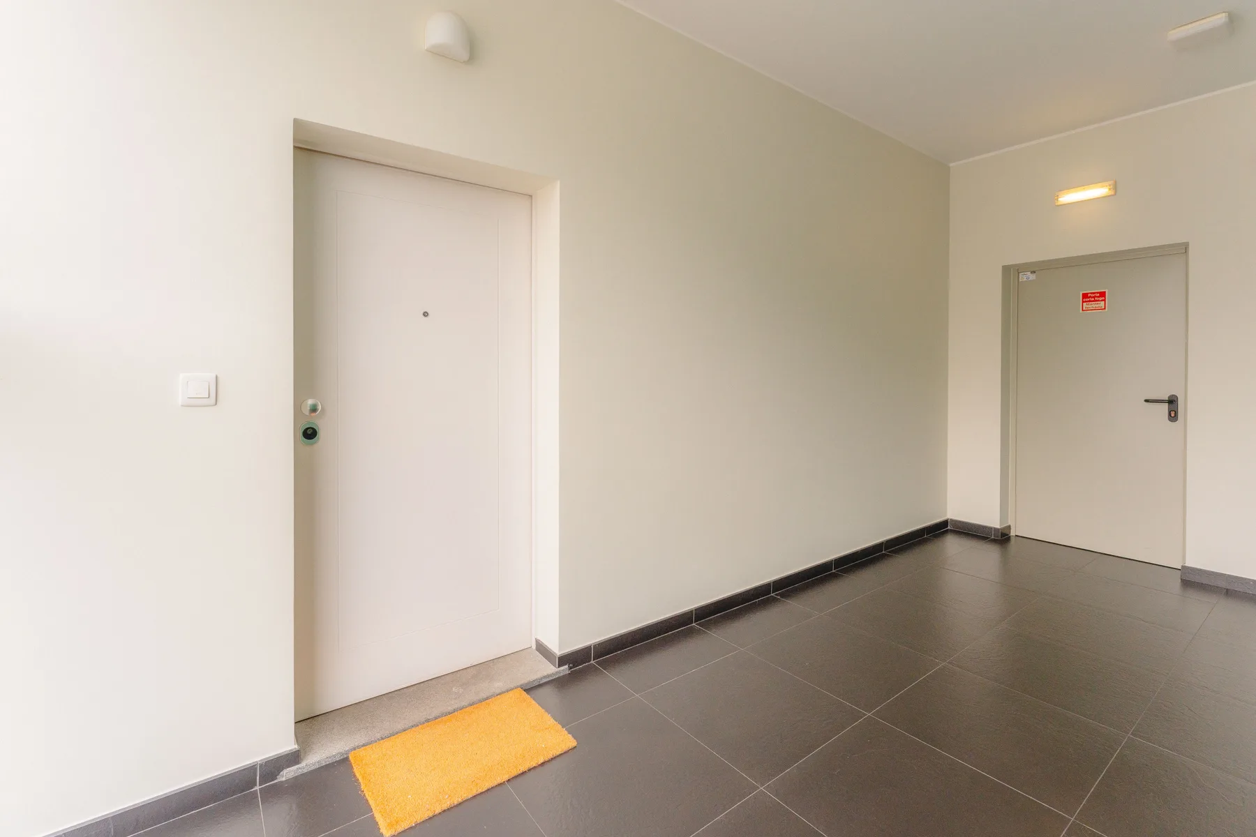 Un pasillo interior con dos puertas y suelo de baldosas oscuras.