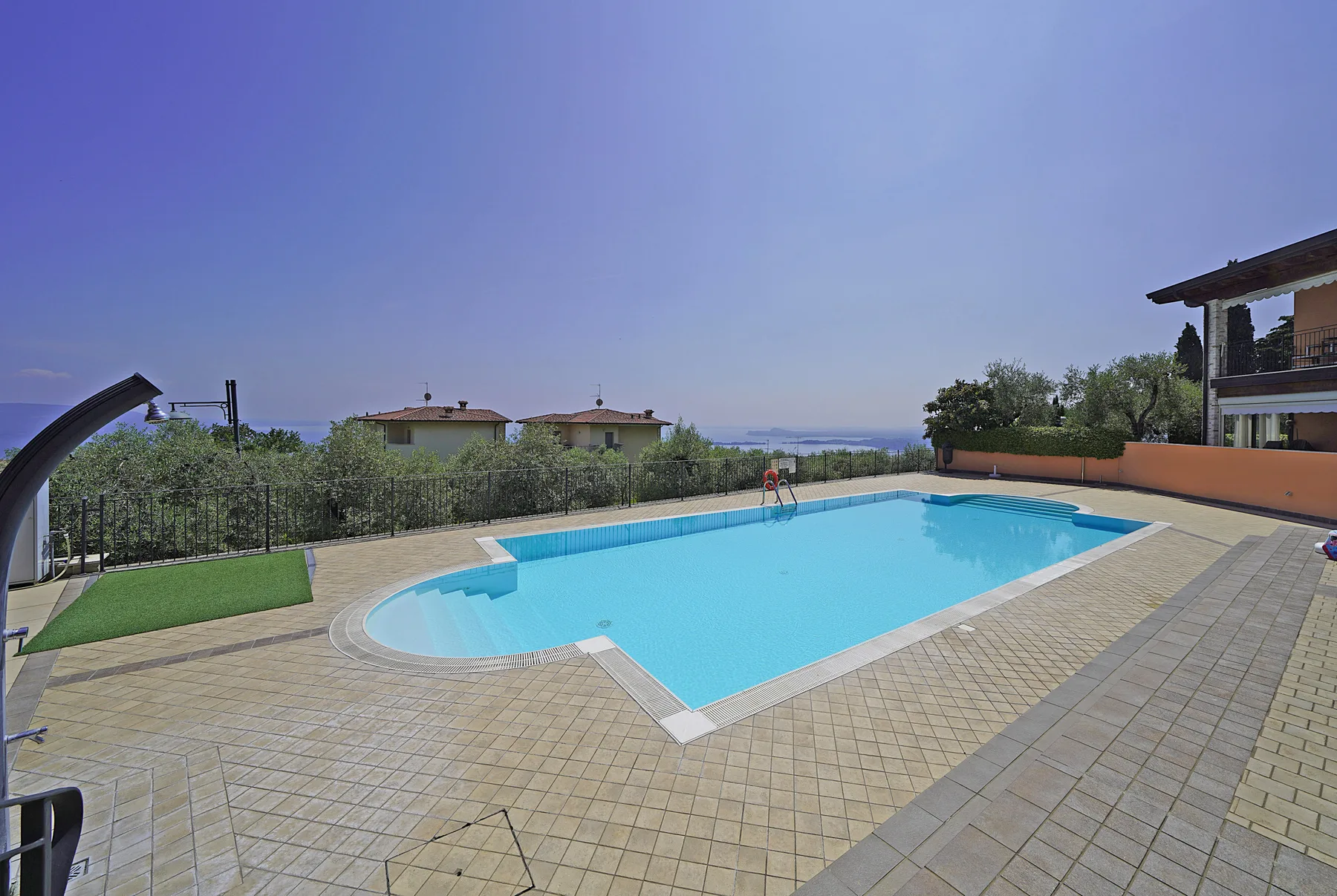 An outdoor swimming pool sits beside a paved patio and landscaped garden.