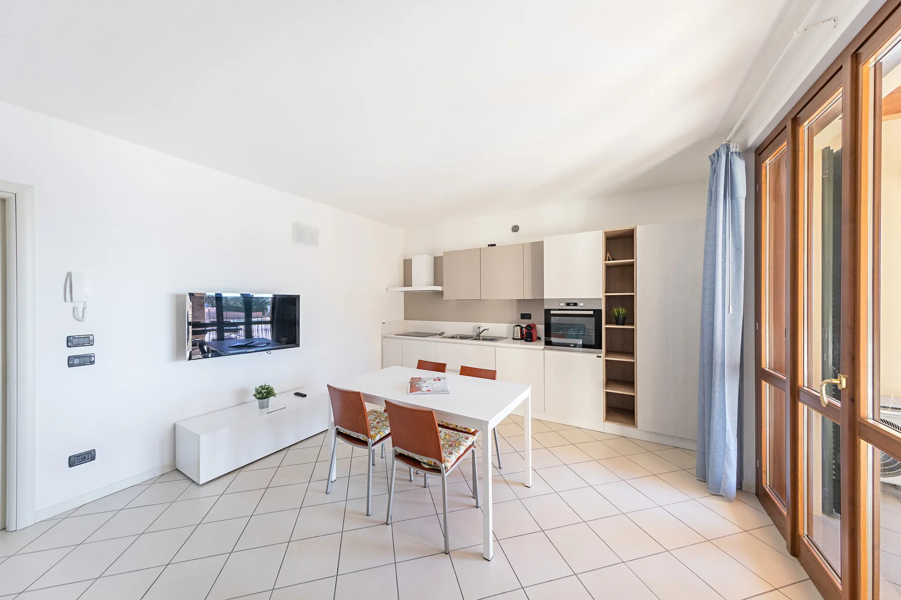 A bright kitchen and dining area with a table, cabinets, and large windows.