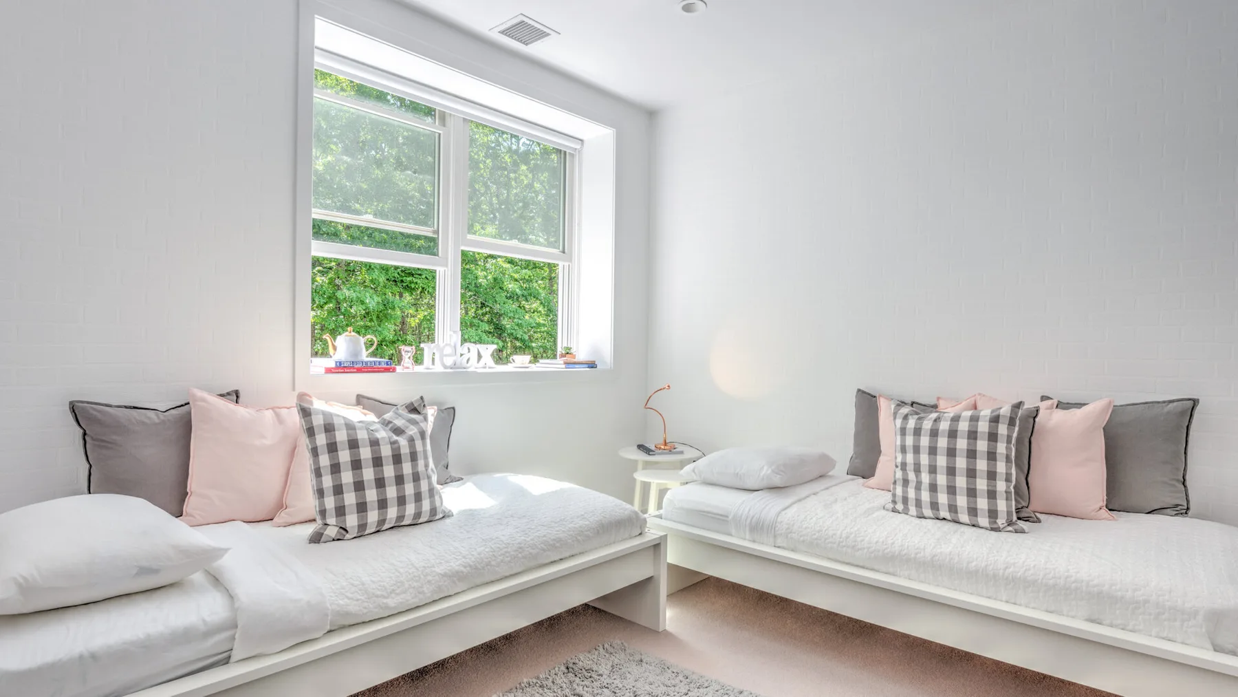 Un dormitorio luminoso con dos camas y una gran ventana con vistas a la vegetación.