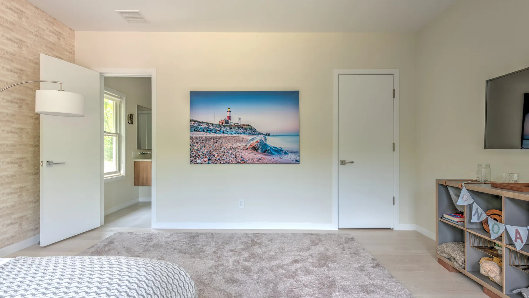 Un dormitorio luminoso con una cama, un televisor en la pared y una imagen costera enmarcada.