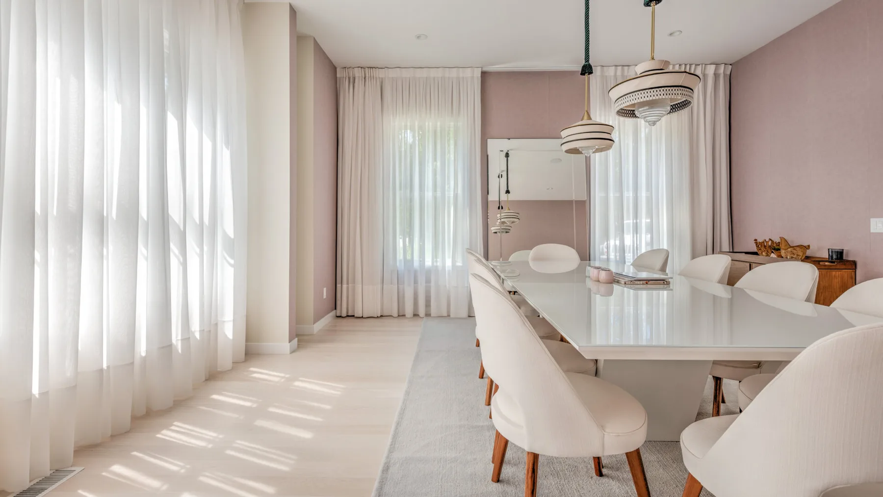 Un comedor luminoso con una mesa larga y asientos tapizados junto a ventanas altas.