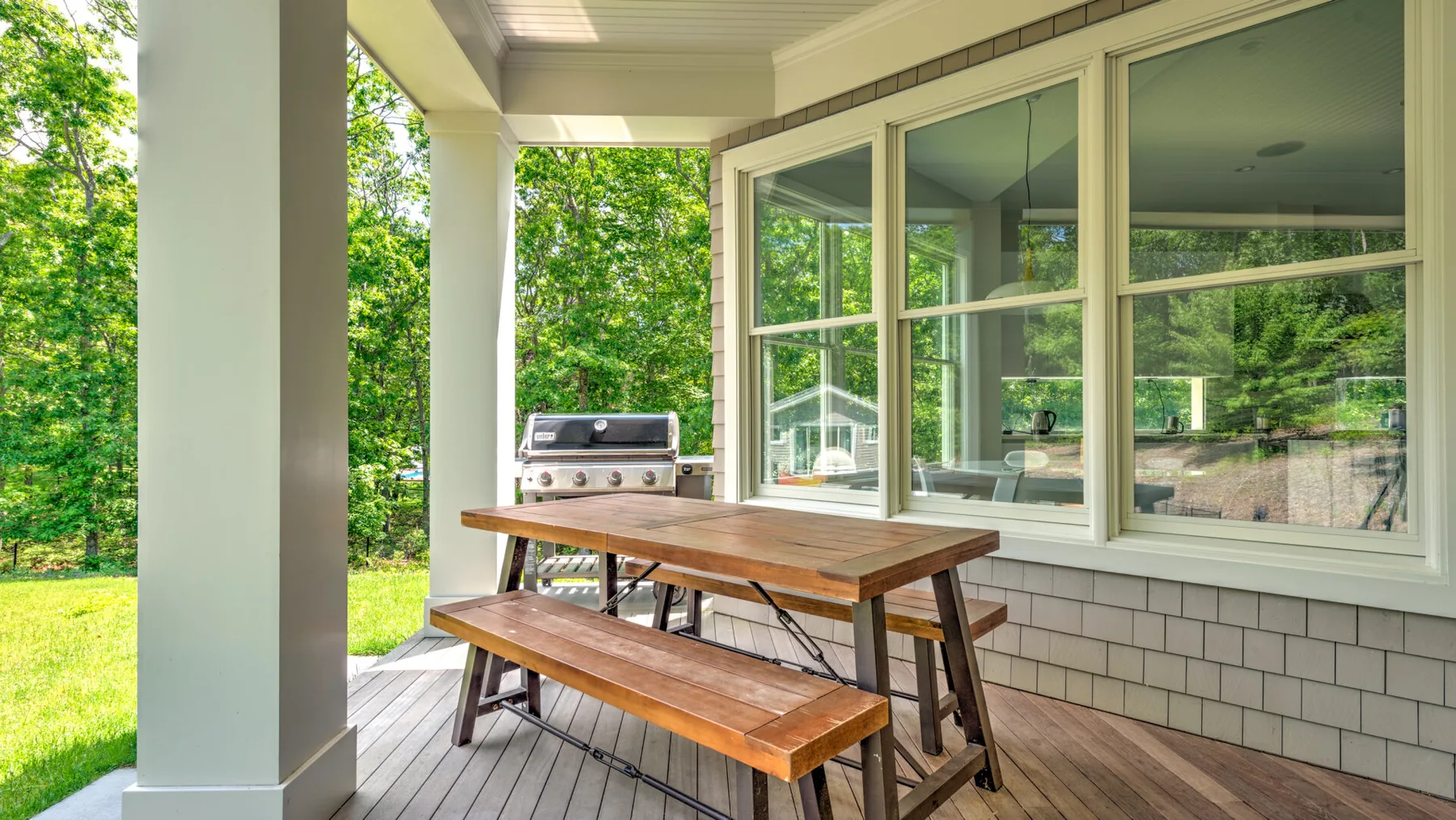 Comedor exterior cubierto con una mesa de madera y un banco junto a grandes ventanas.