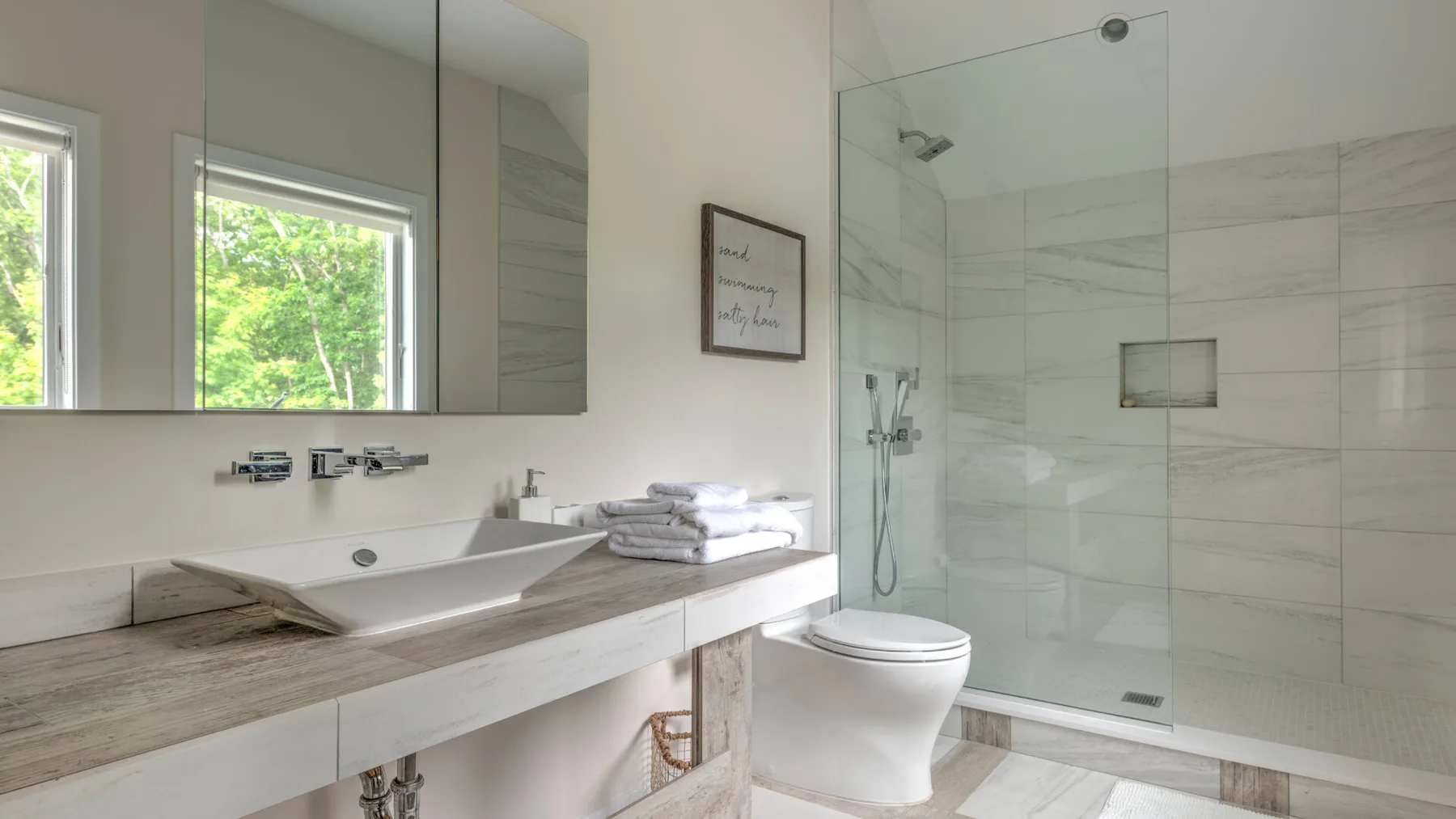 Un baño luminoso con un tocador largo, un lavabo y una ducha de cristal.