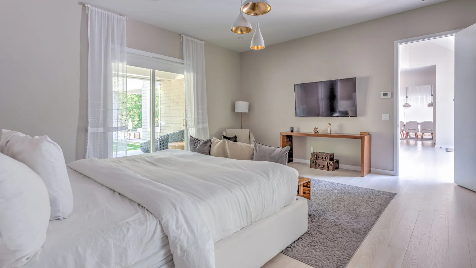 Un dormitorio luminoso con una cama grande, un televisor en la pared y una puerta corrediza de vidrio.