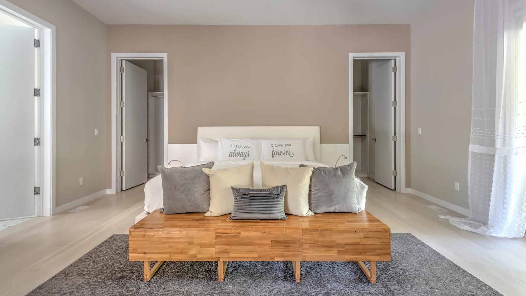 Un dormitorio con una cama, un banco de madera y una alfombra gris.