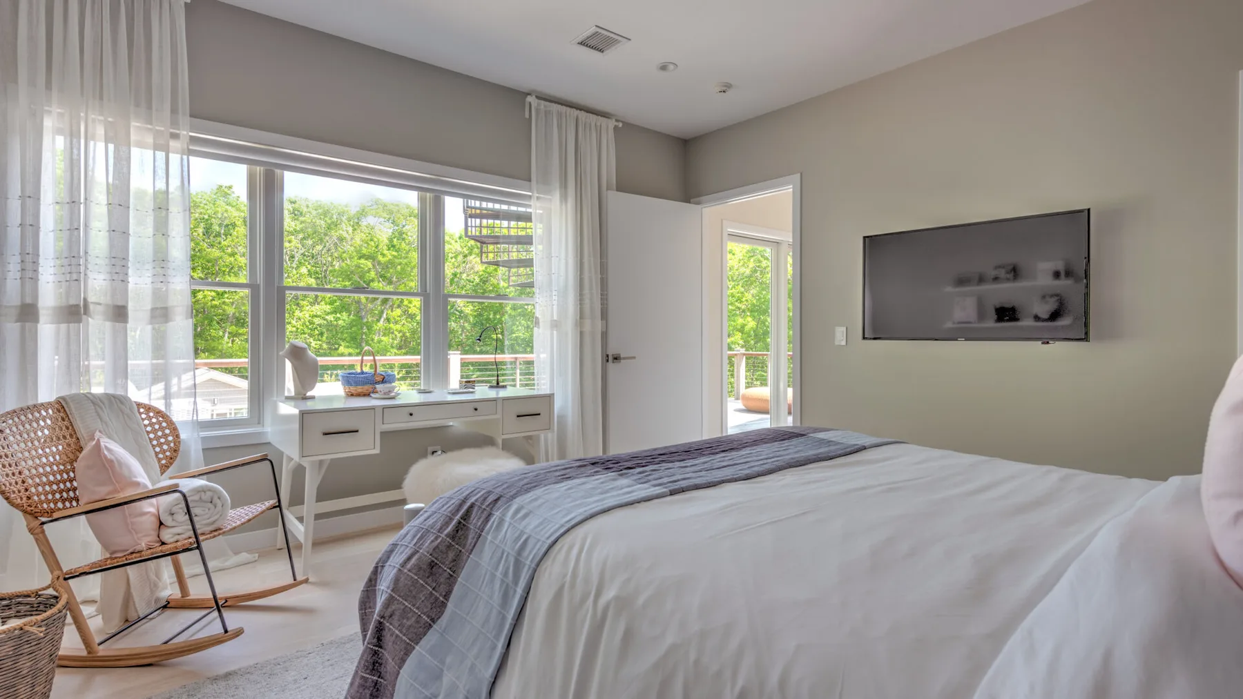 Un dormitorio luminoso con una ventana amplia y un televisor en la pared.