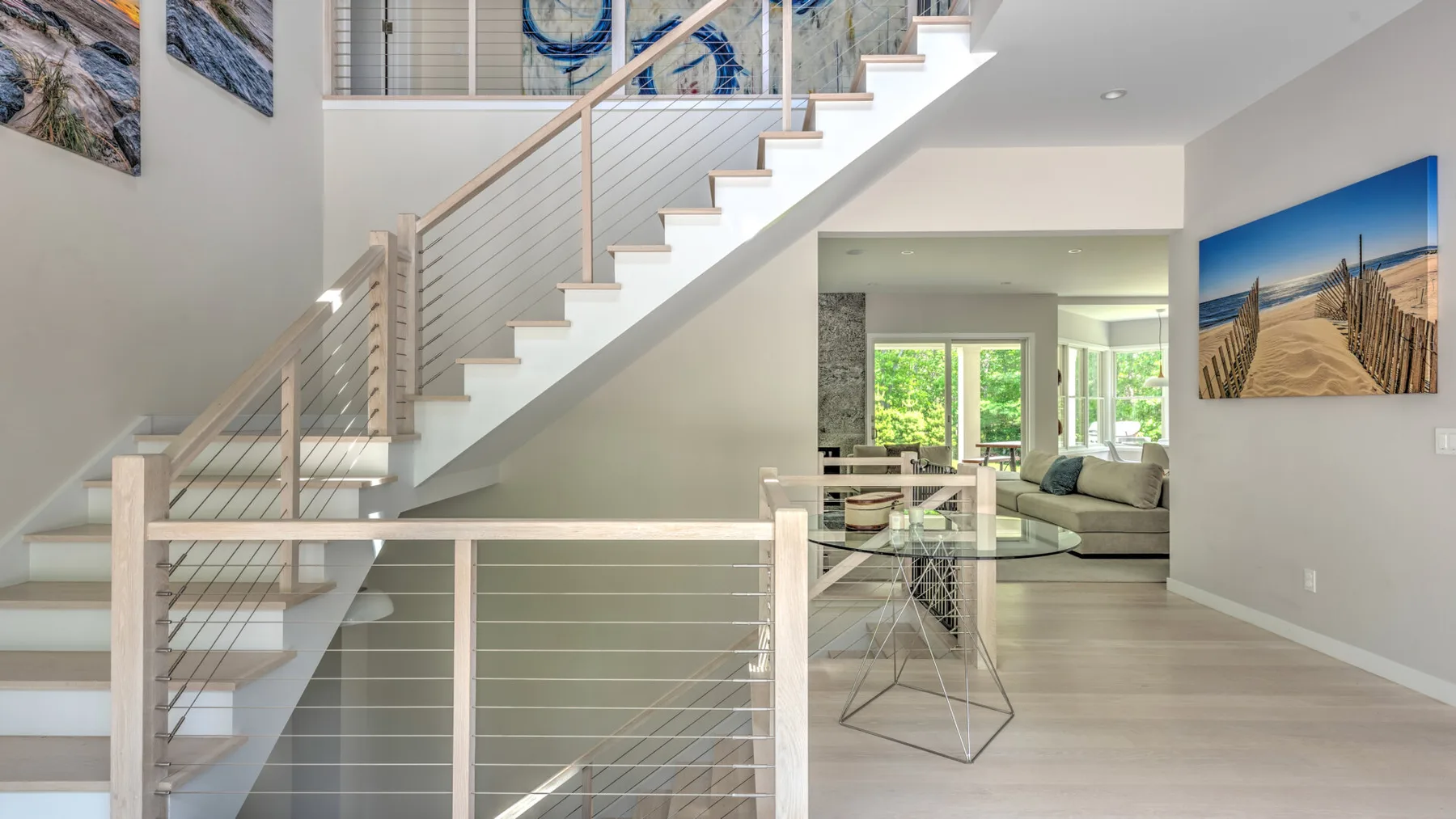 Una luminosa sala de estar con una escalera, una mesa de comedor de vidrio y asientos junto a las ventanas.