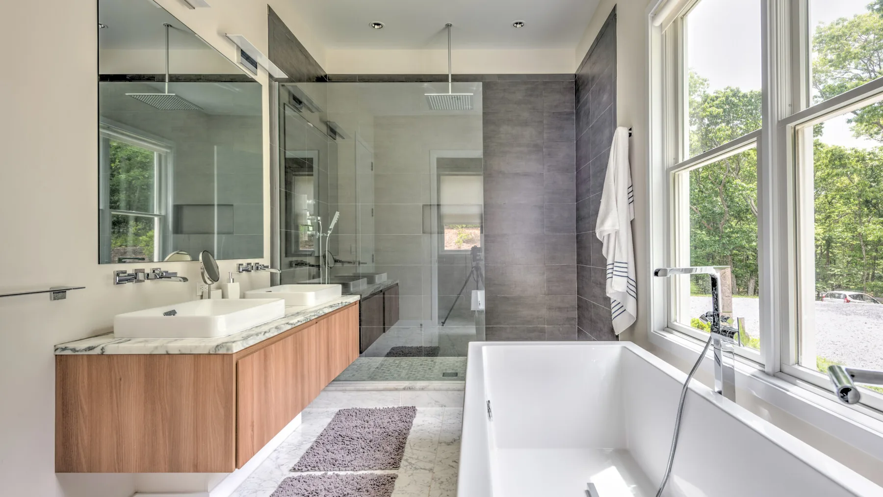 Un baño moderno con un tocador largo, una ducha de vidrio y una bañera independiente.