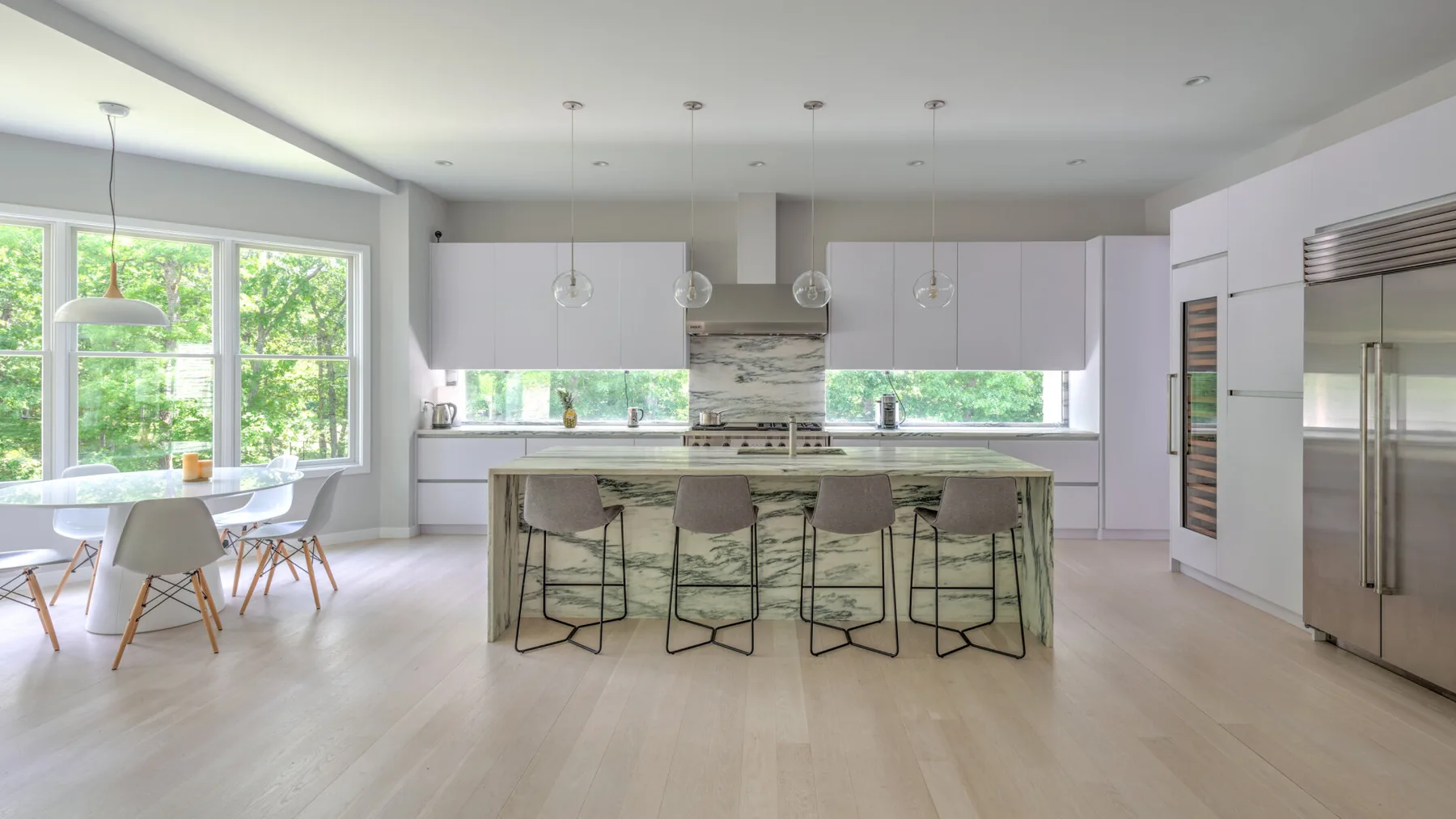 Una cocina abierta y luminosa con isla y comedor junto a grandes ventanas.