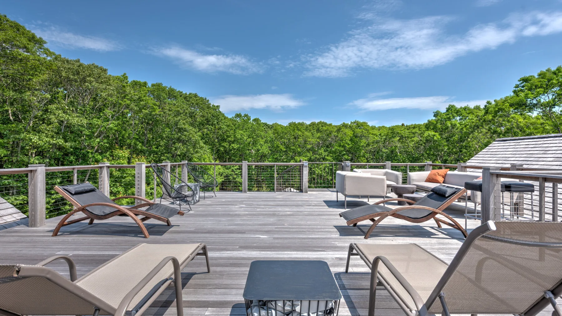 A spacious outdoor deck has lounge seating and overlooks a green tree canopy.